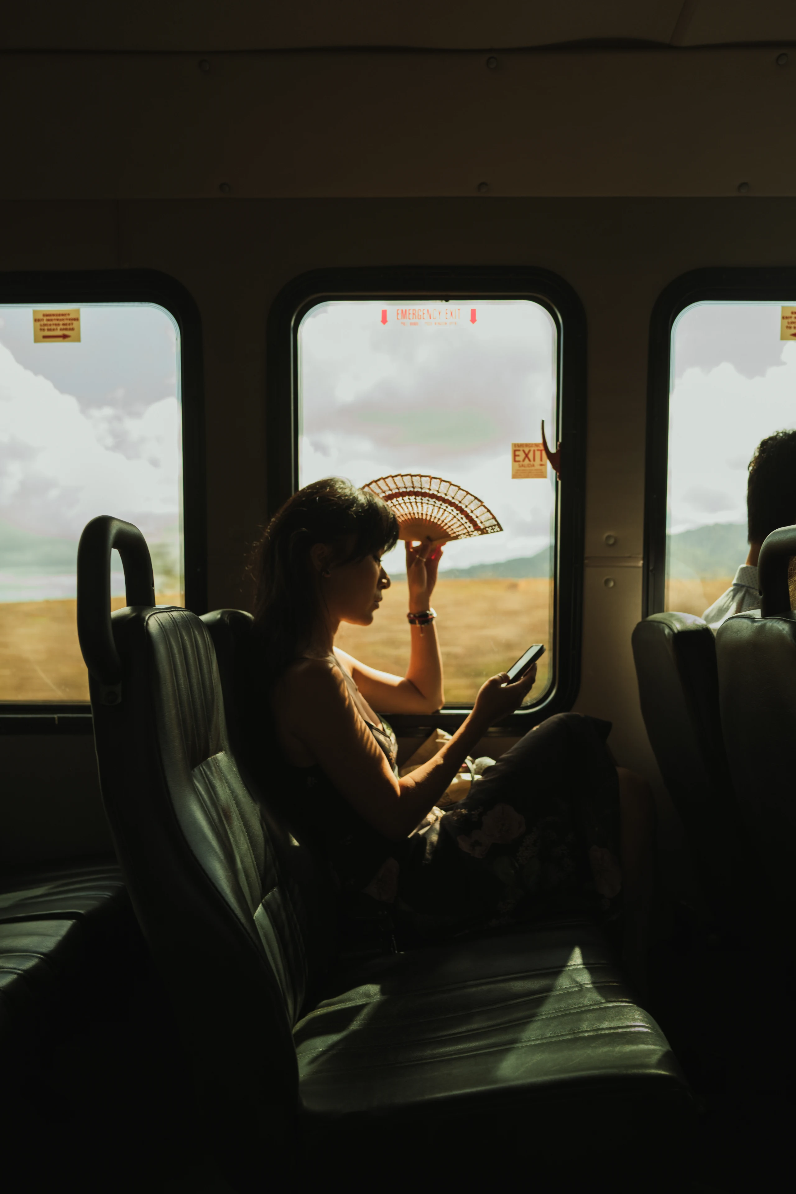 Woman seated on a city bus in sunlight, framed by its windows.