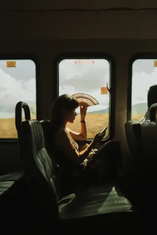 Woman seated on a city bus in sunlight, framed by its windows.