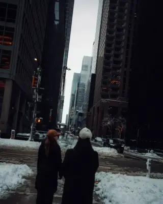 Two people walking through a snow-lined Midtown intersection