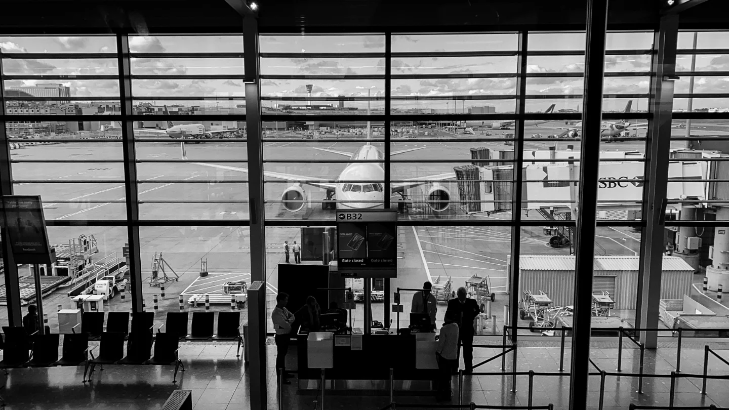 An airplane parked at an airport gate beyond a wall of gridded windows, with staff and empty seats below.