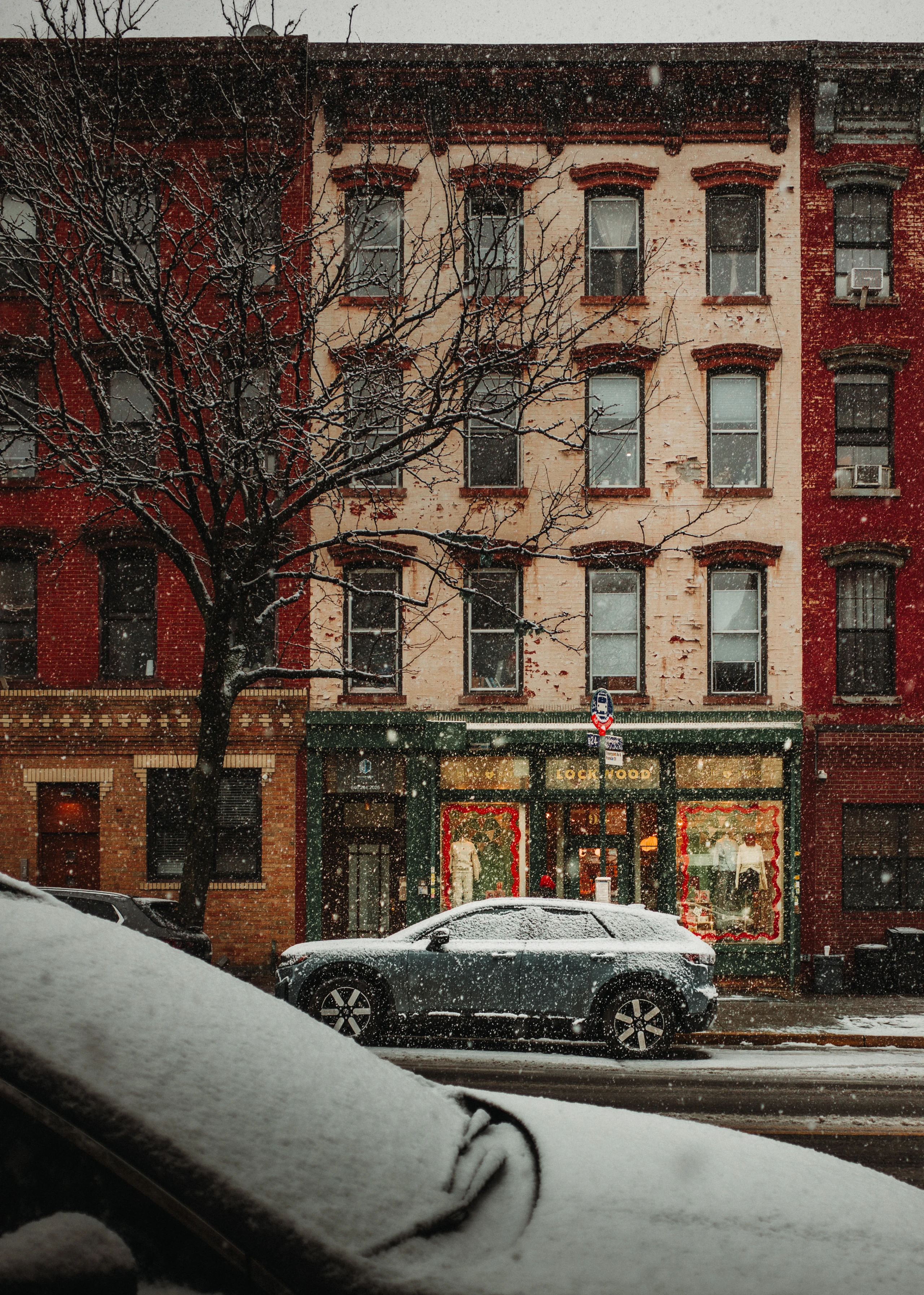 Snow coats parked cars along a New York street lined with brick and pale apartment facades.
