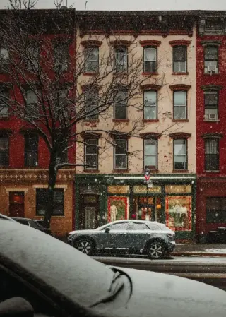 Snow coats parked cars along a New York street lined with brick and pale apartment facades.