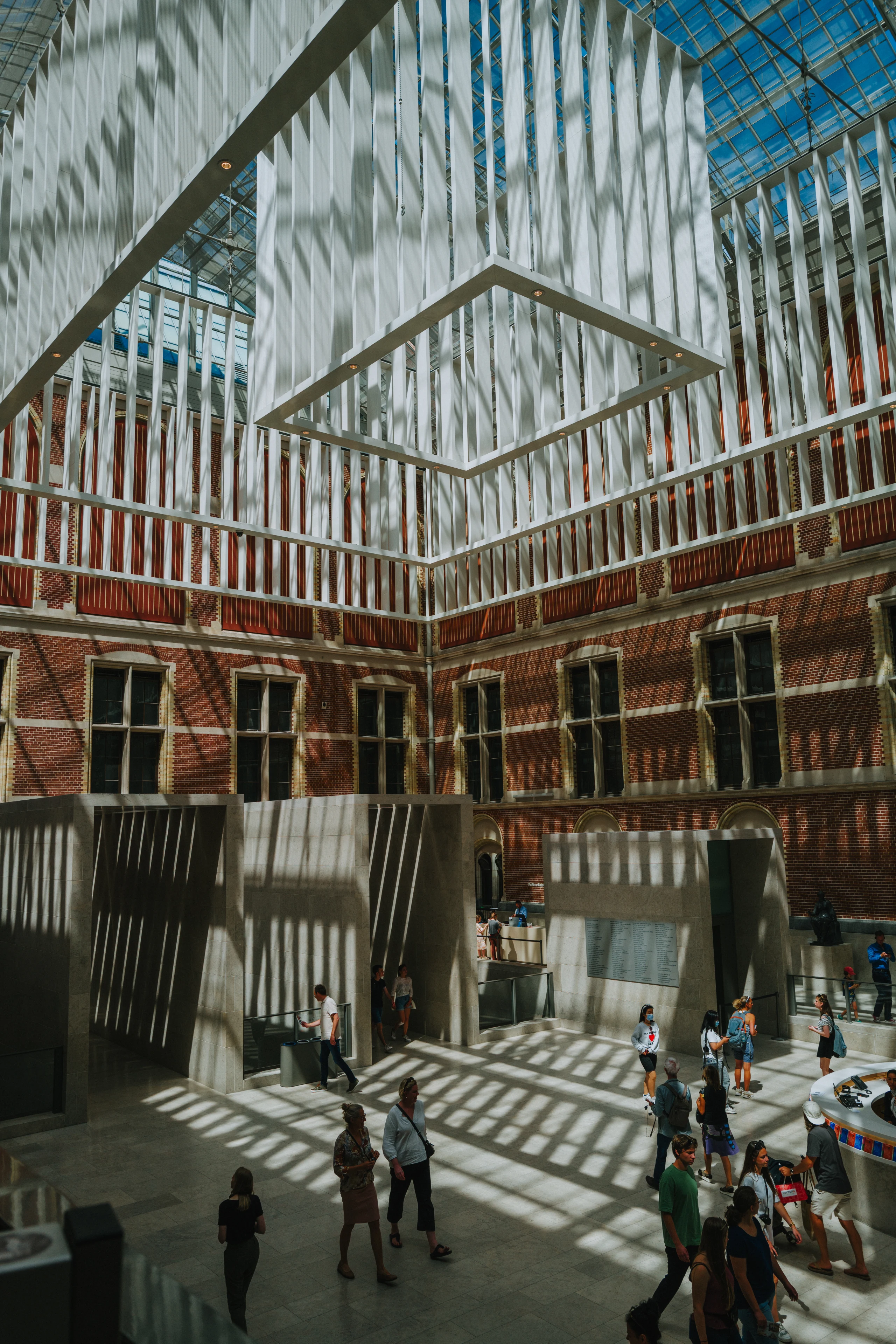 Visitors cross the Rijksmuseum atrium beneath white suspended structures and a geometric pattern of sunlight.