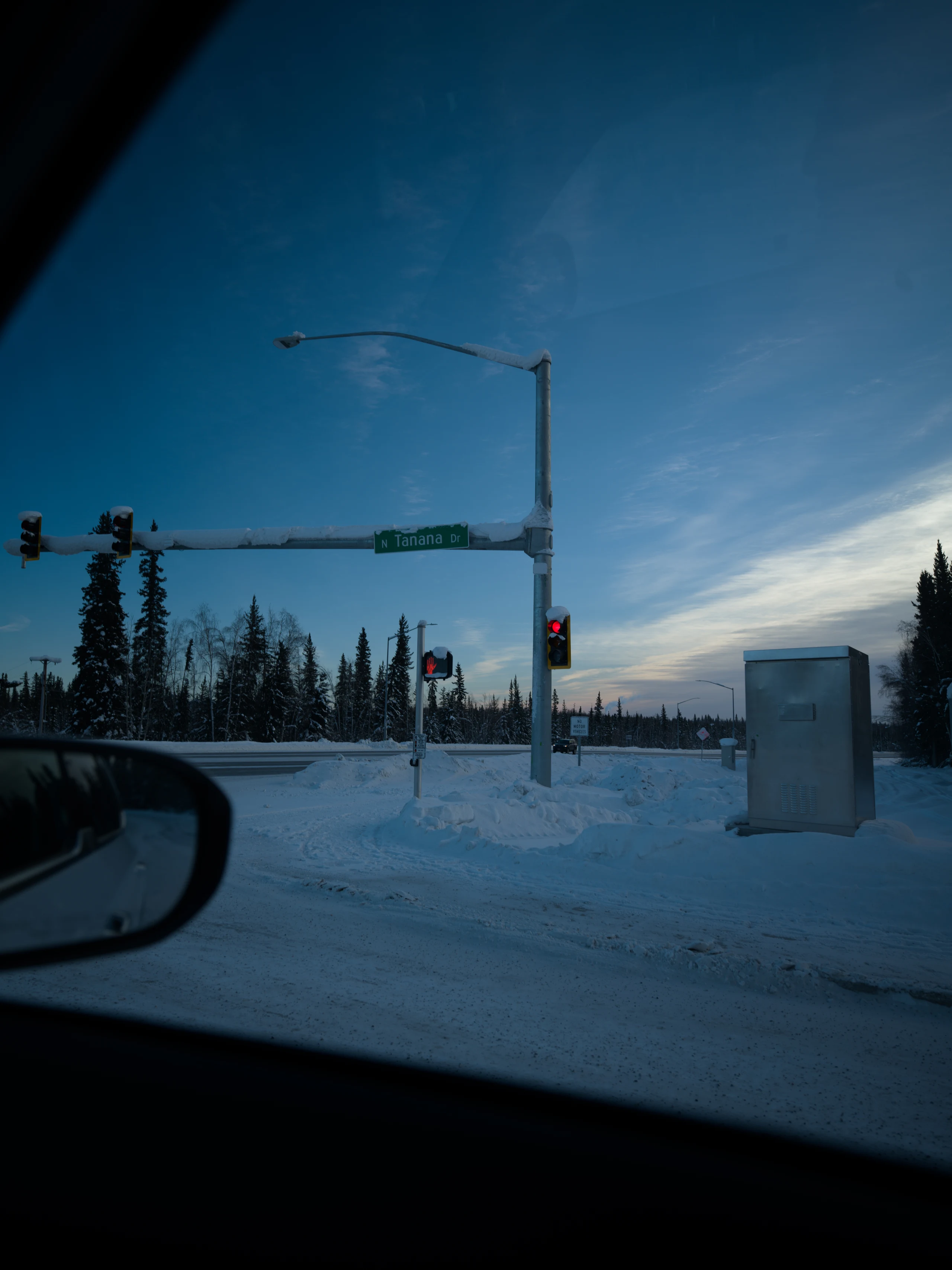A snowy road and traffic light seen through a car windshield in blue evening light.