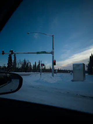 A snowy road and traffic light seen through a car windshield in blue evening light.