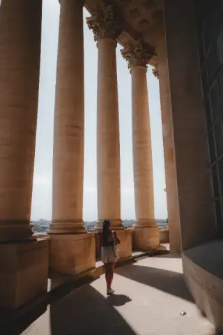 Lone figure passing between monumental sunlit columns.