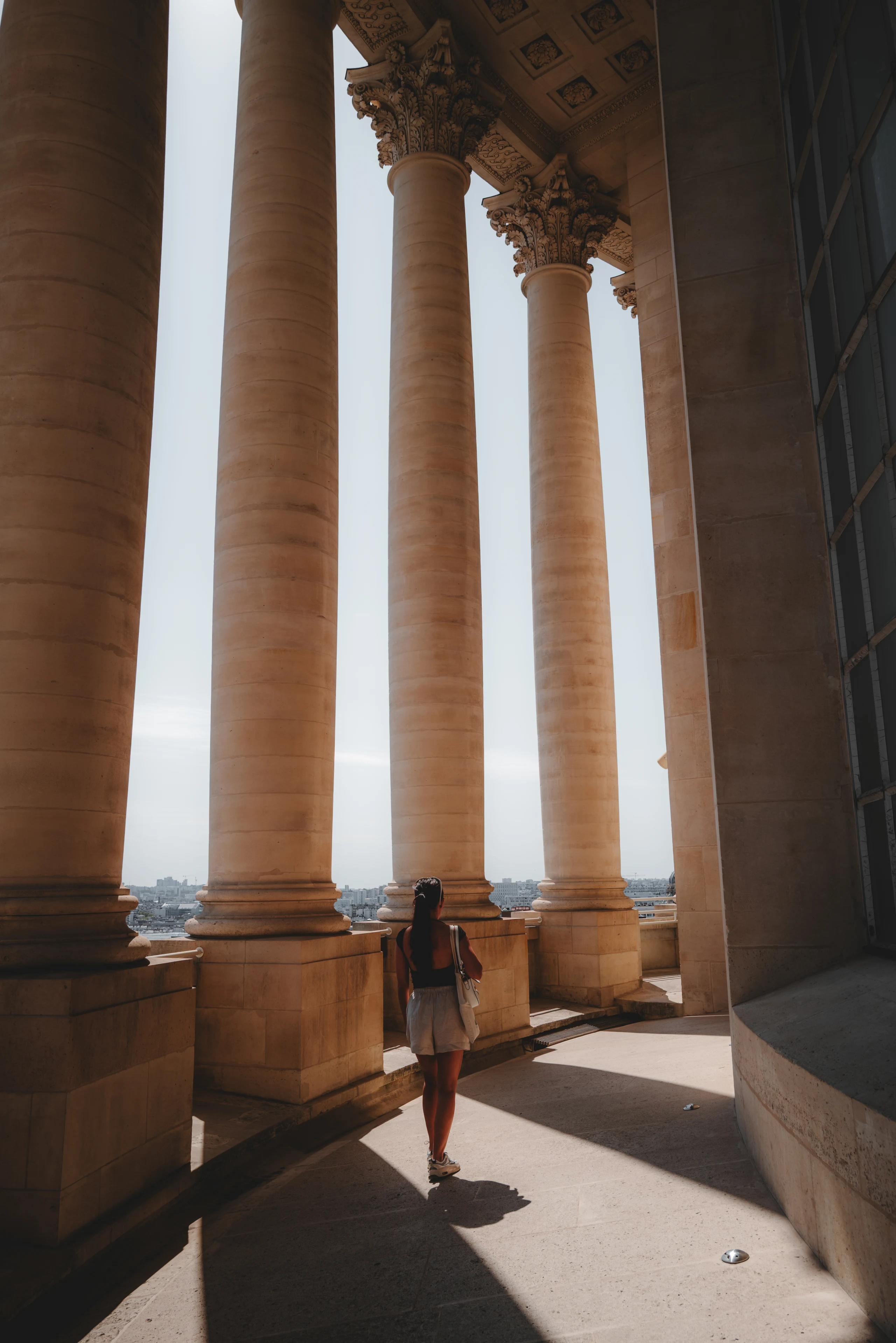 Lone figure passing between monumental sunlit columns.