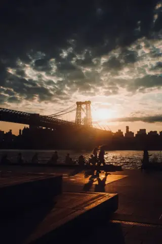 The Williamsburg Bridge is silhouetted against a golden sunset.