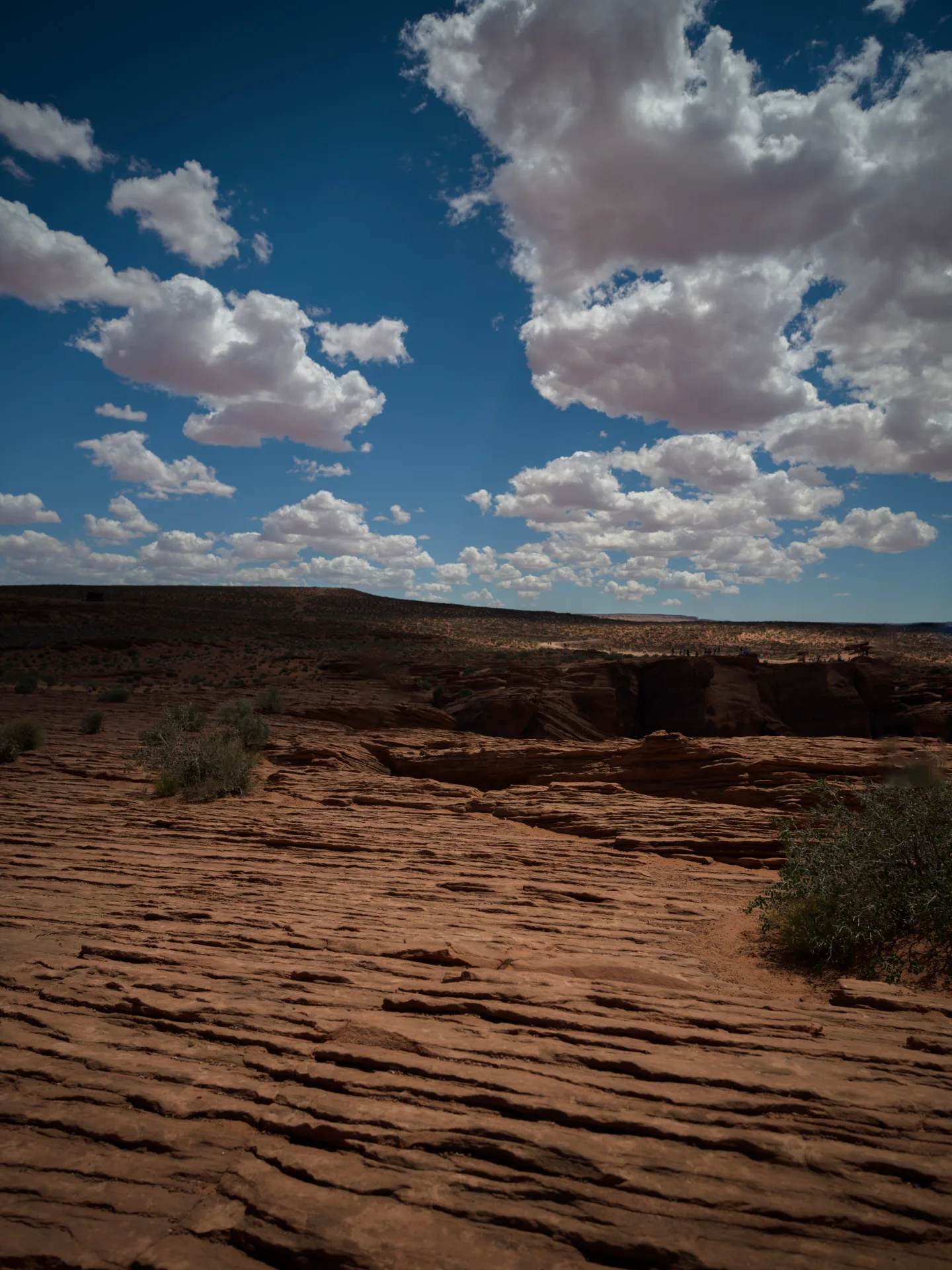 Layered red sandstone shelves descend into a dark desert hollow beneath cumulus clouds.