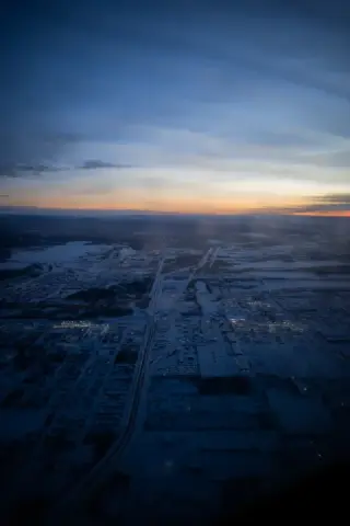 An aerial view shows a snow-covered Alaska town beneath a blue and orange winter sunset.