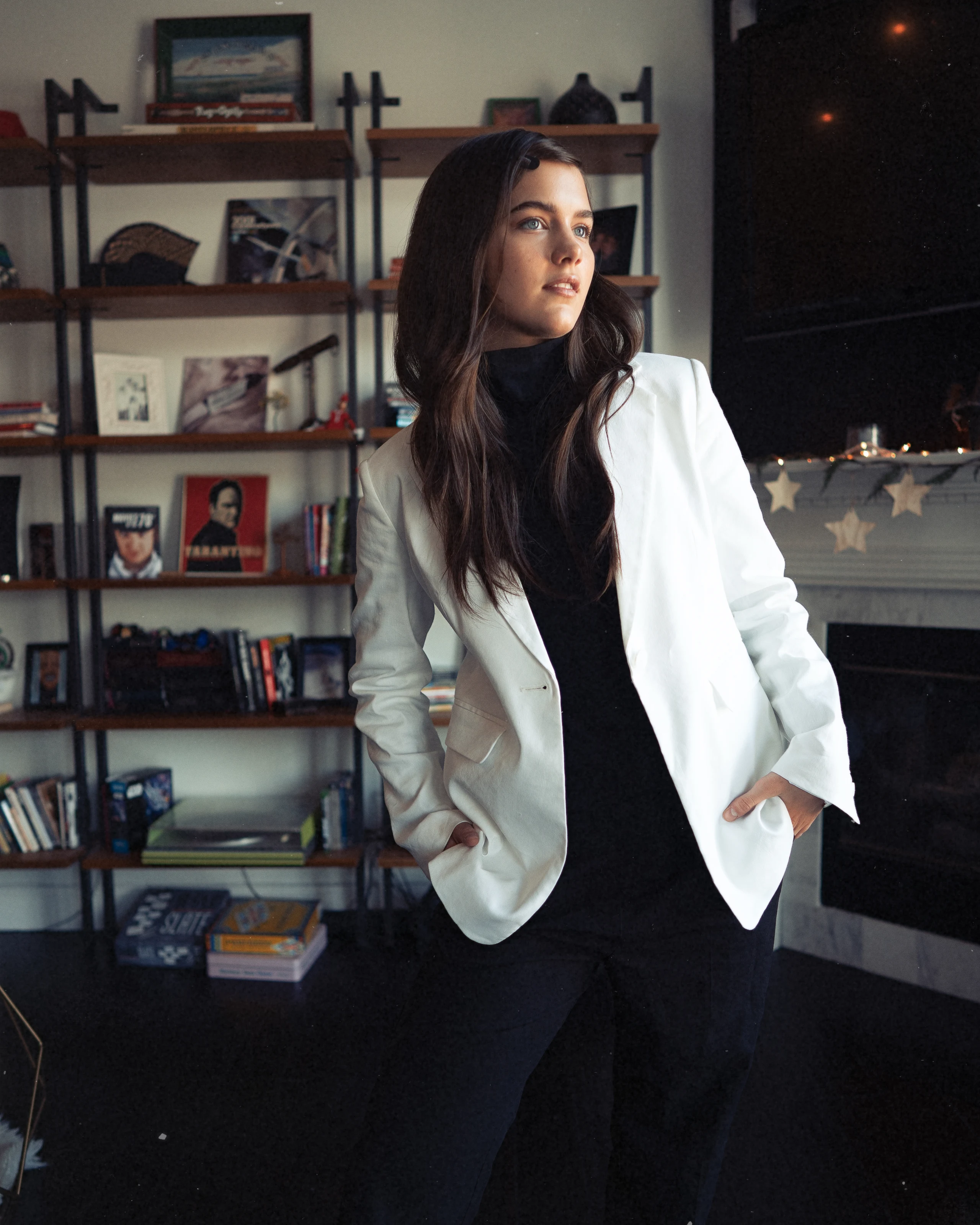 A woman in a white suit standing in a room lined with records and books.