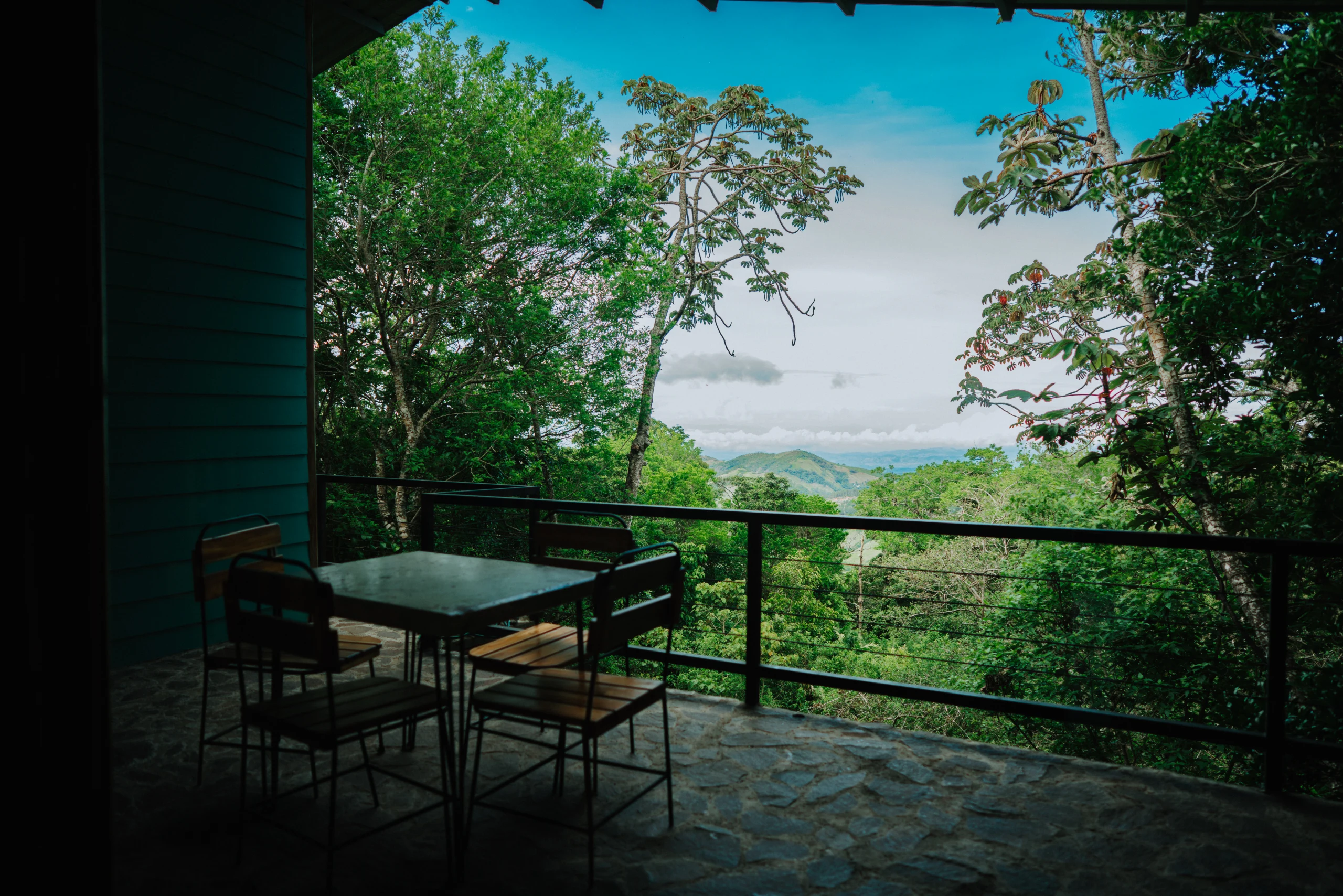 A stone terrace with a table overlooks layered green hills and distant sky.
