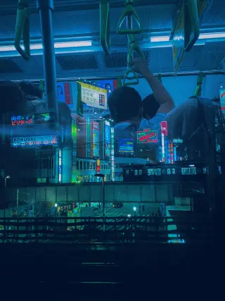 A passenger grips an overhead strap inside a train, reflected over blue neon signs and another train outside in Takadanobaba.