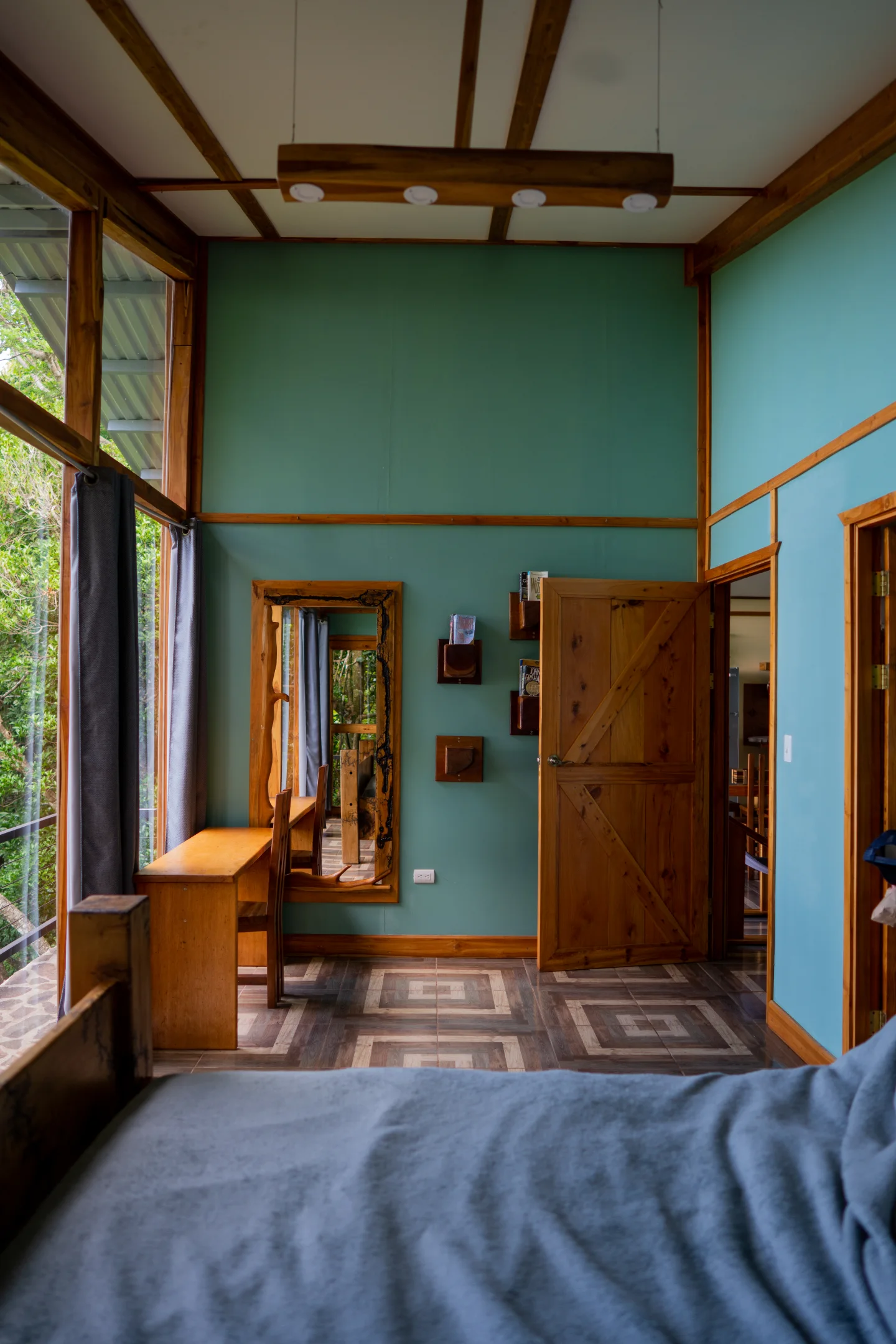 A timber-framed bedroom opens through a doorway toward dense tropical greenery.