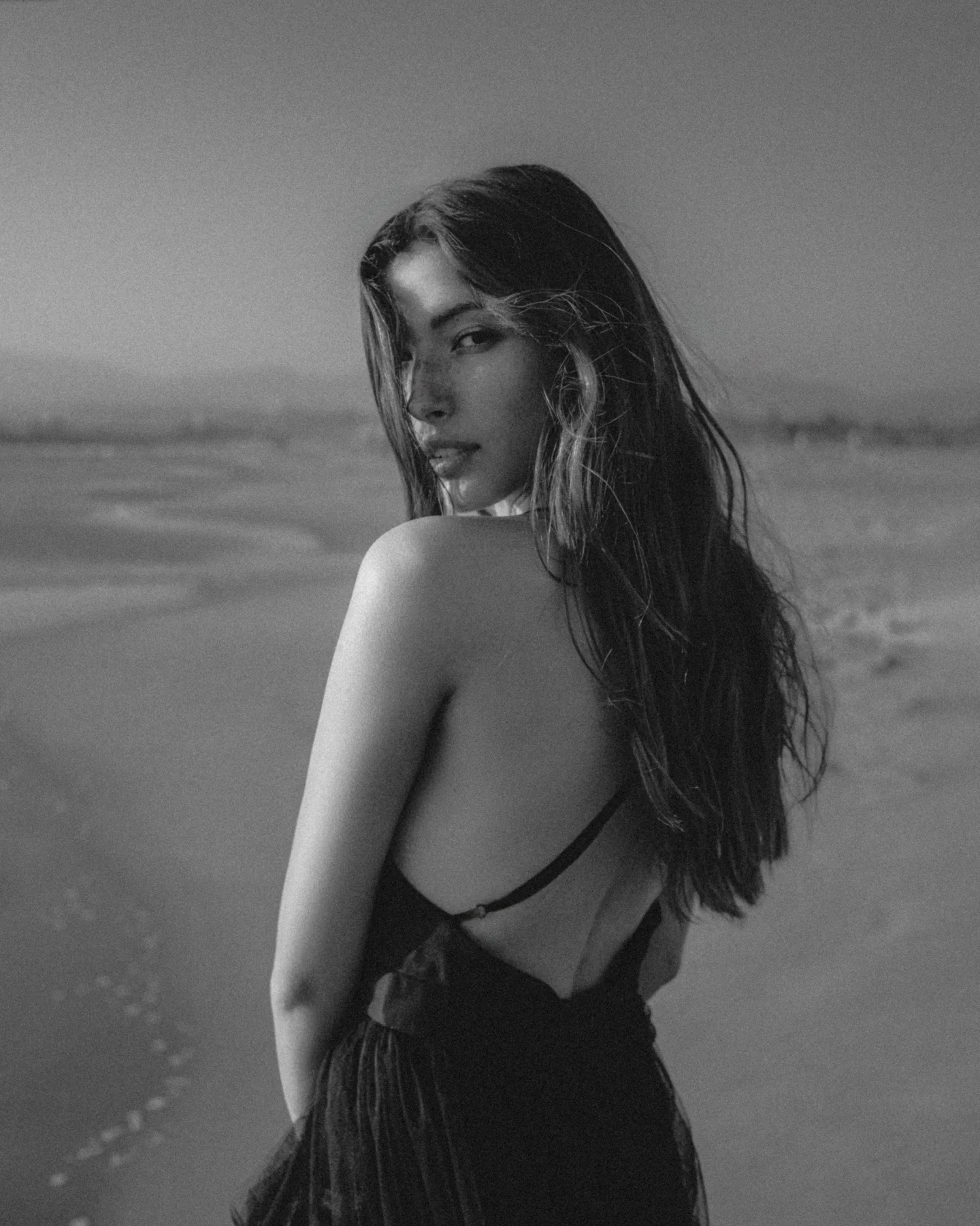 Black-and-white portrait of a woman looking back over her shoulder on a beach.