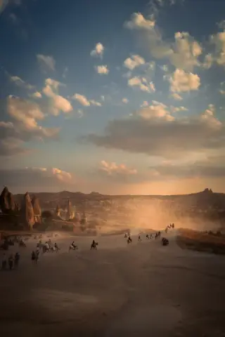 Dust hangs above a line of ATV riders crossing an open Cappadocia plain beneath warm clouds.