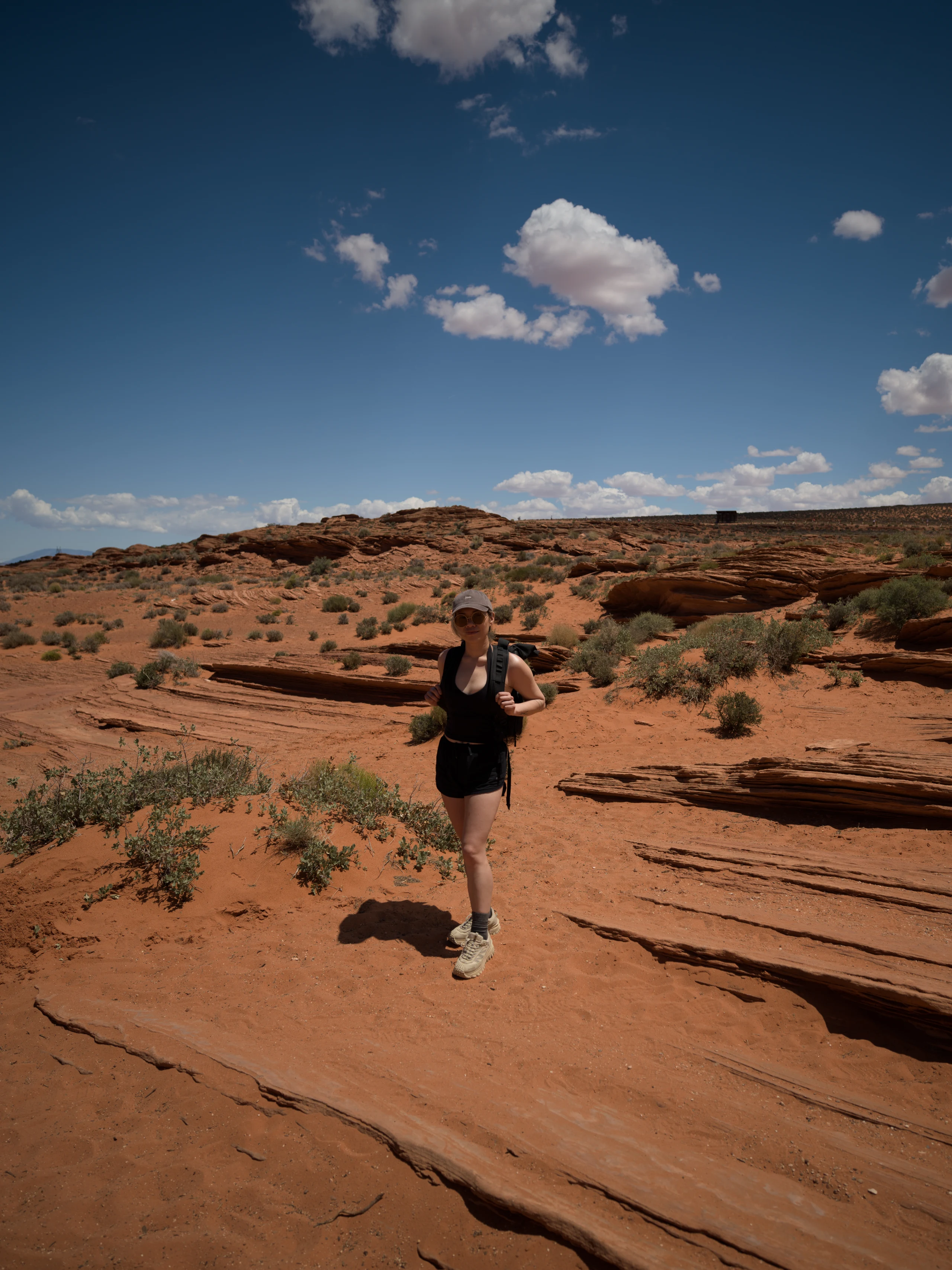 A person walks across red sandstone beneath scattered clouds.