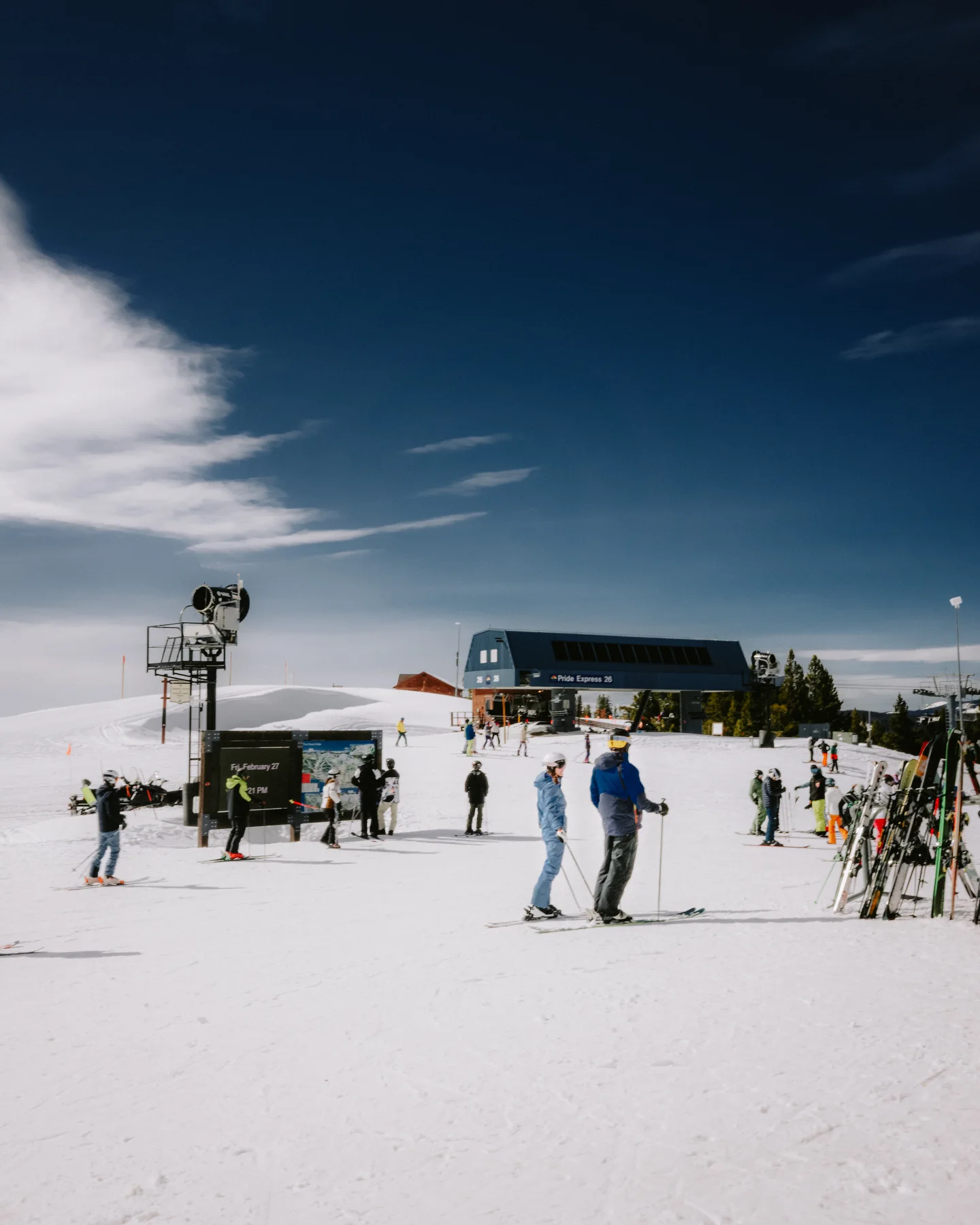 Skiers waiting near the Pride Express chairlift terminal beneath a deep blue sky.