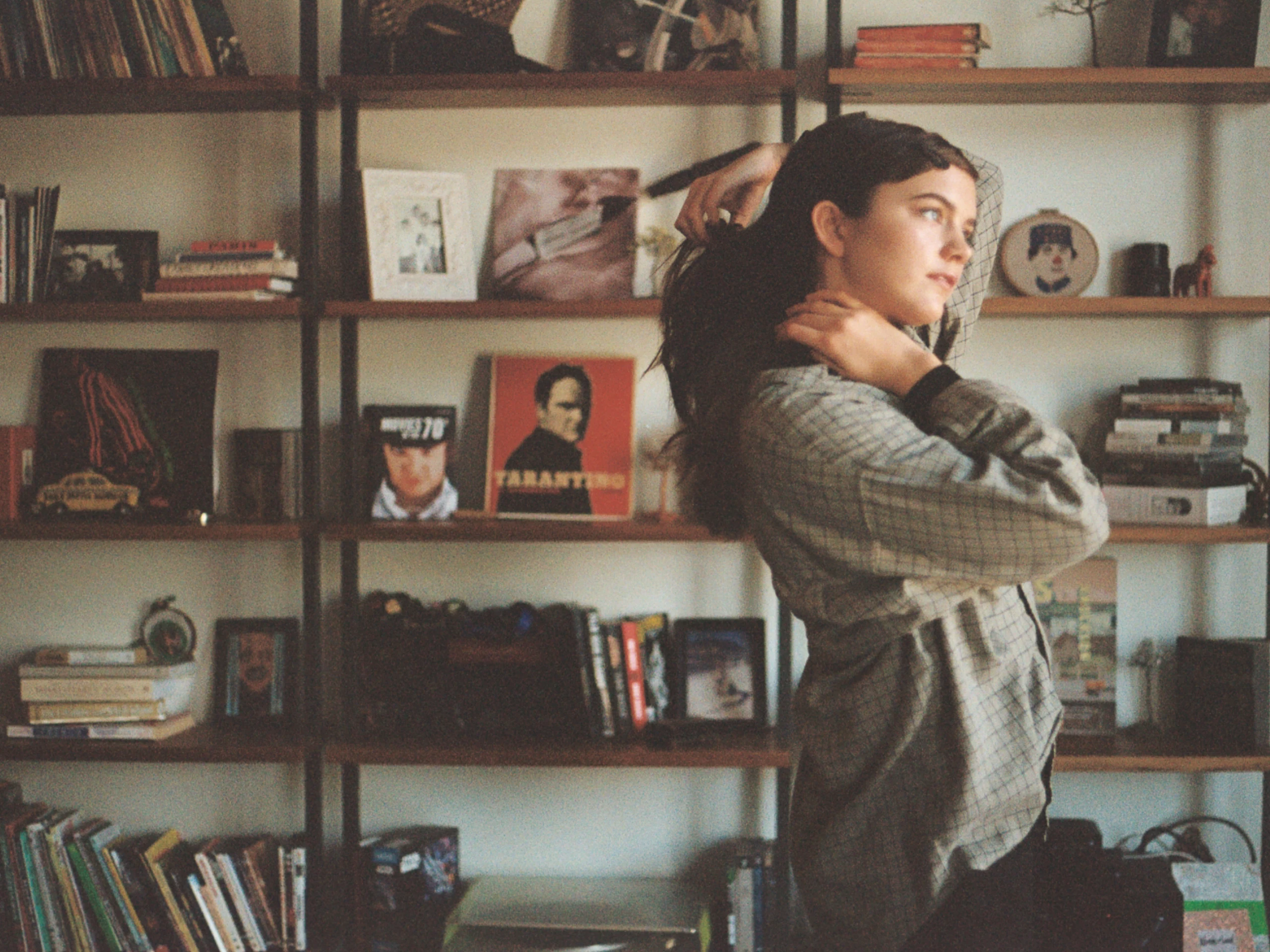 A woman in a loose gray sweater standing before shelves of books and framed photographs.