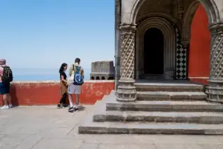 Visitors stand beside a striped arch and deep shadowed doorway.