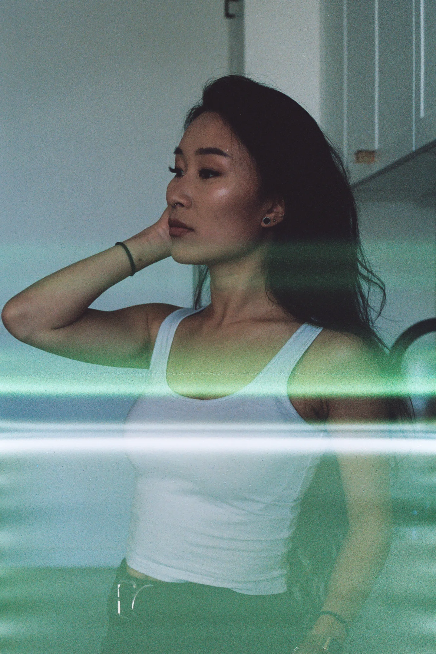 A woman in a white top seen through green-tinted reflective glass.