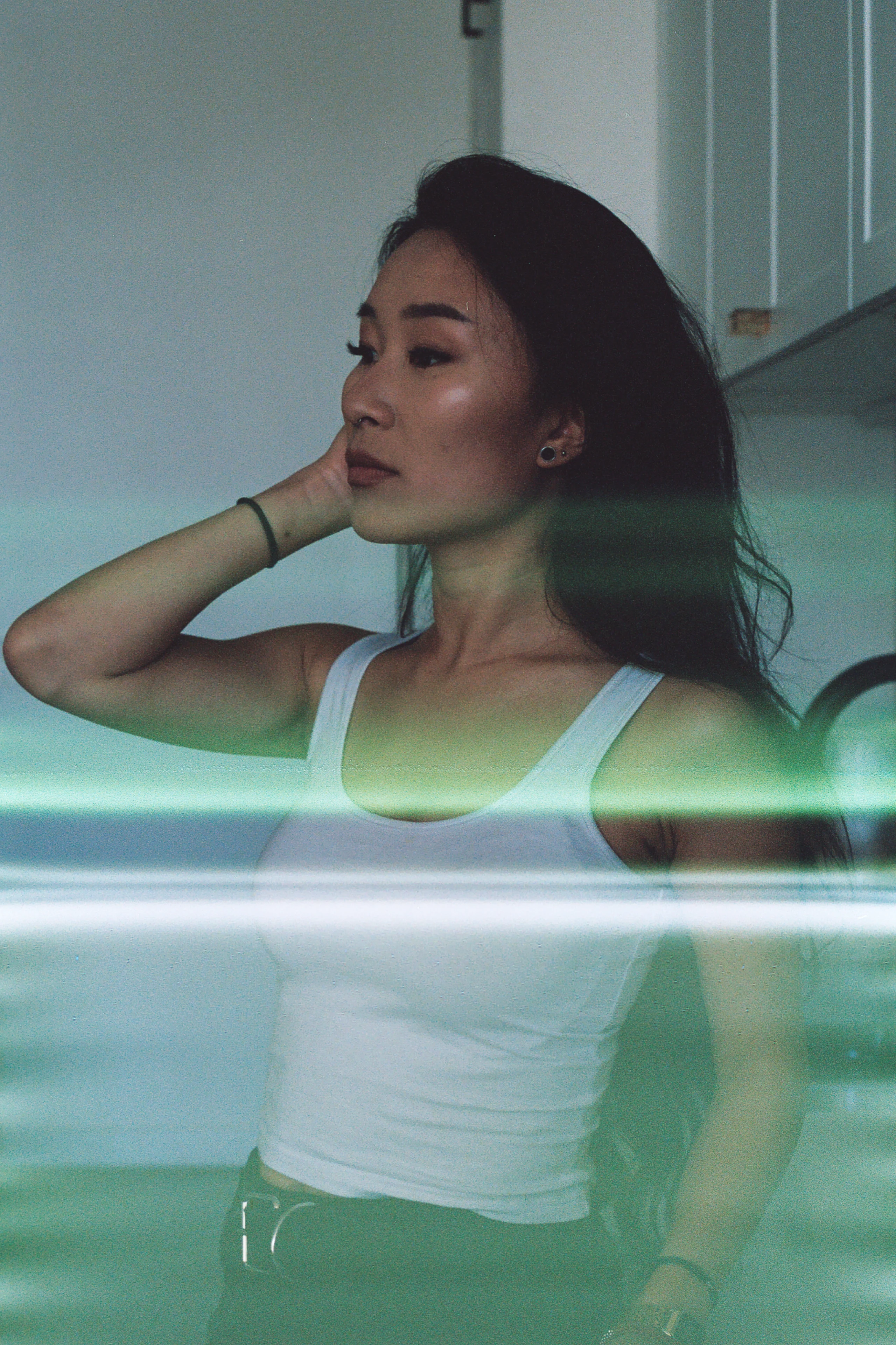 A woman in a white top seen through green-tinted reflective glass.