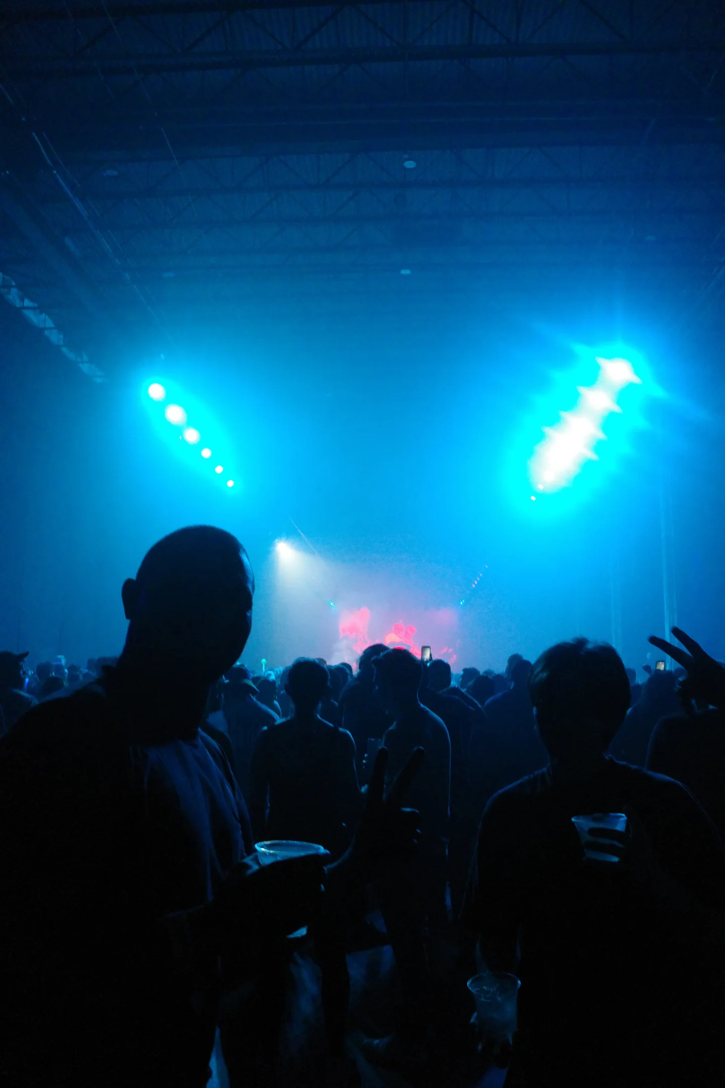 A dense concert crowd in silhouette beneath two bright blue stage lights.