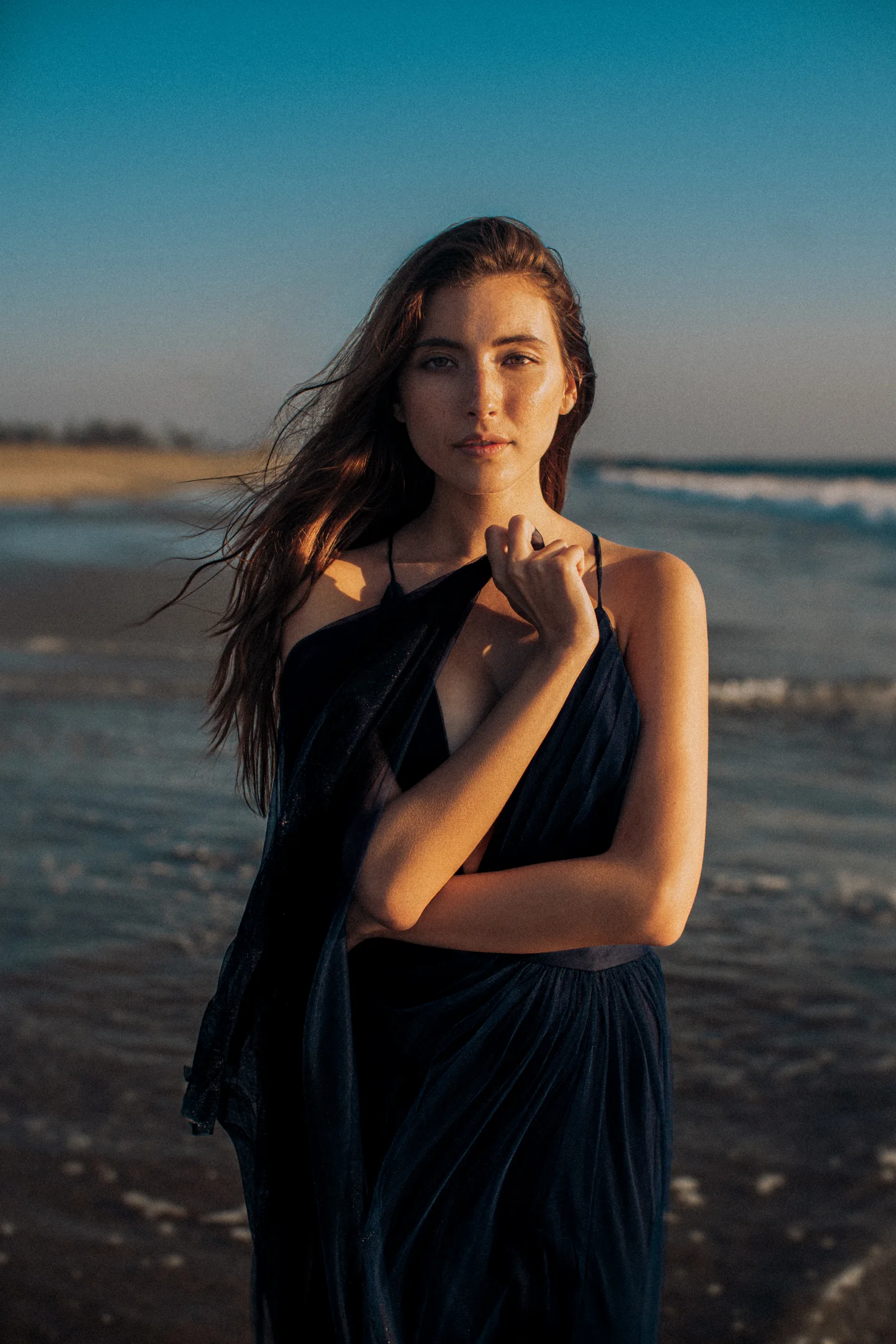 Woman standing with crossed arms at the shoreline.