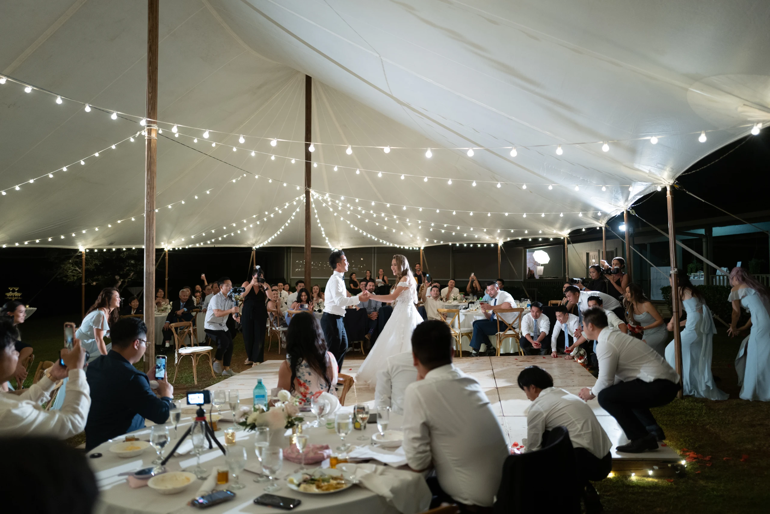 Wedding guests seated beneath a tent and string lights.