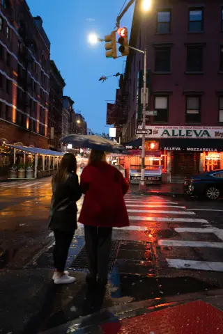 People crossing a wet city street at night beneath red storefront lights.