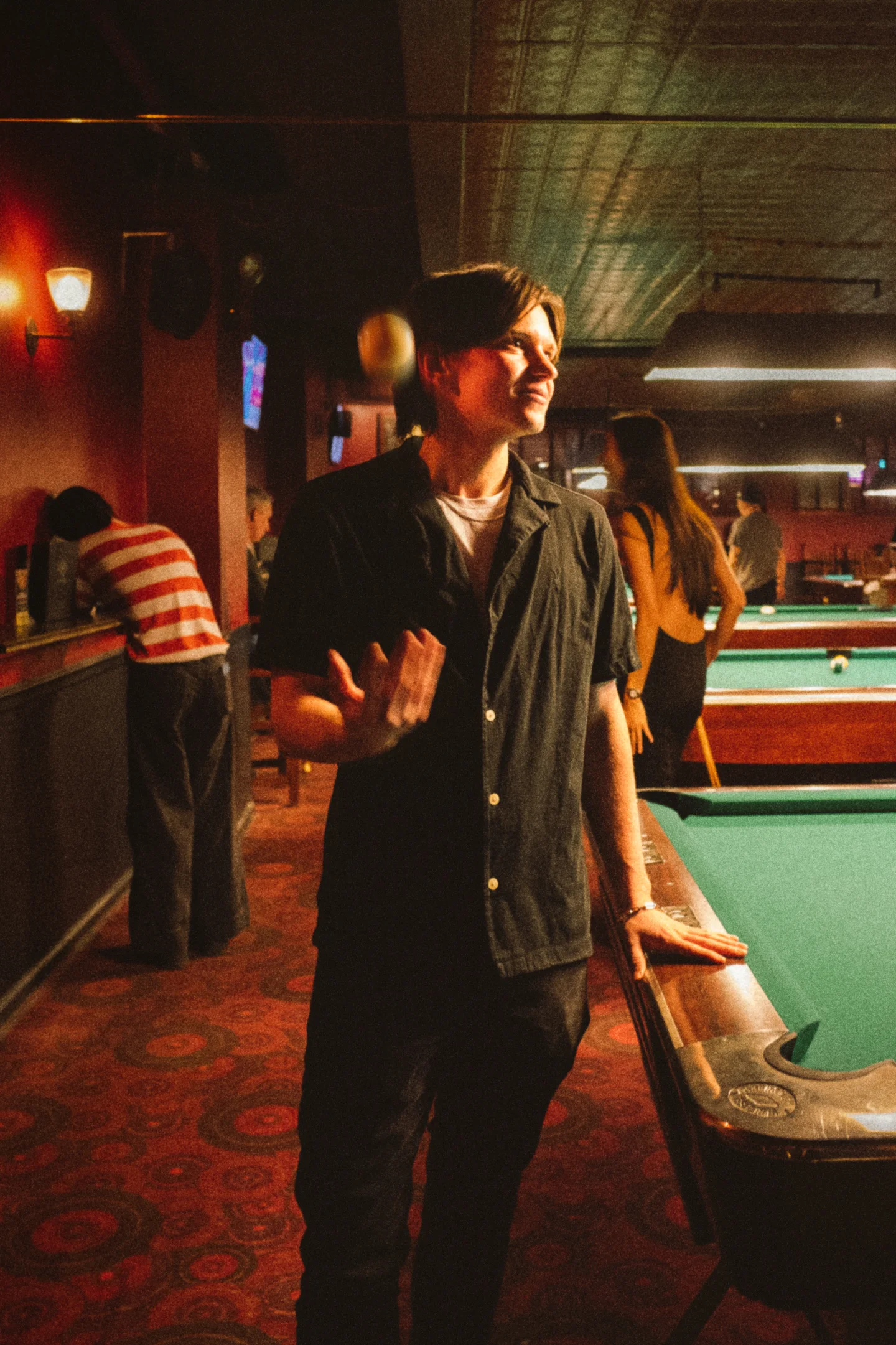 A man stands beside a pool table in a warm, dimly lit room.
