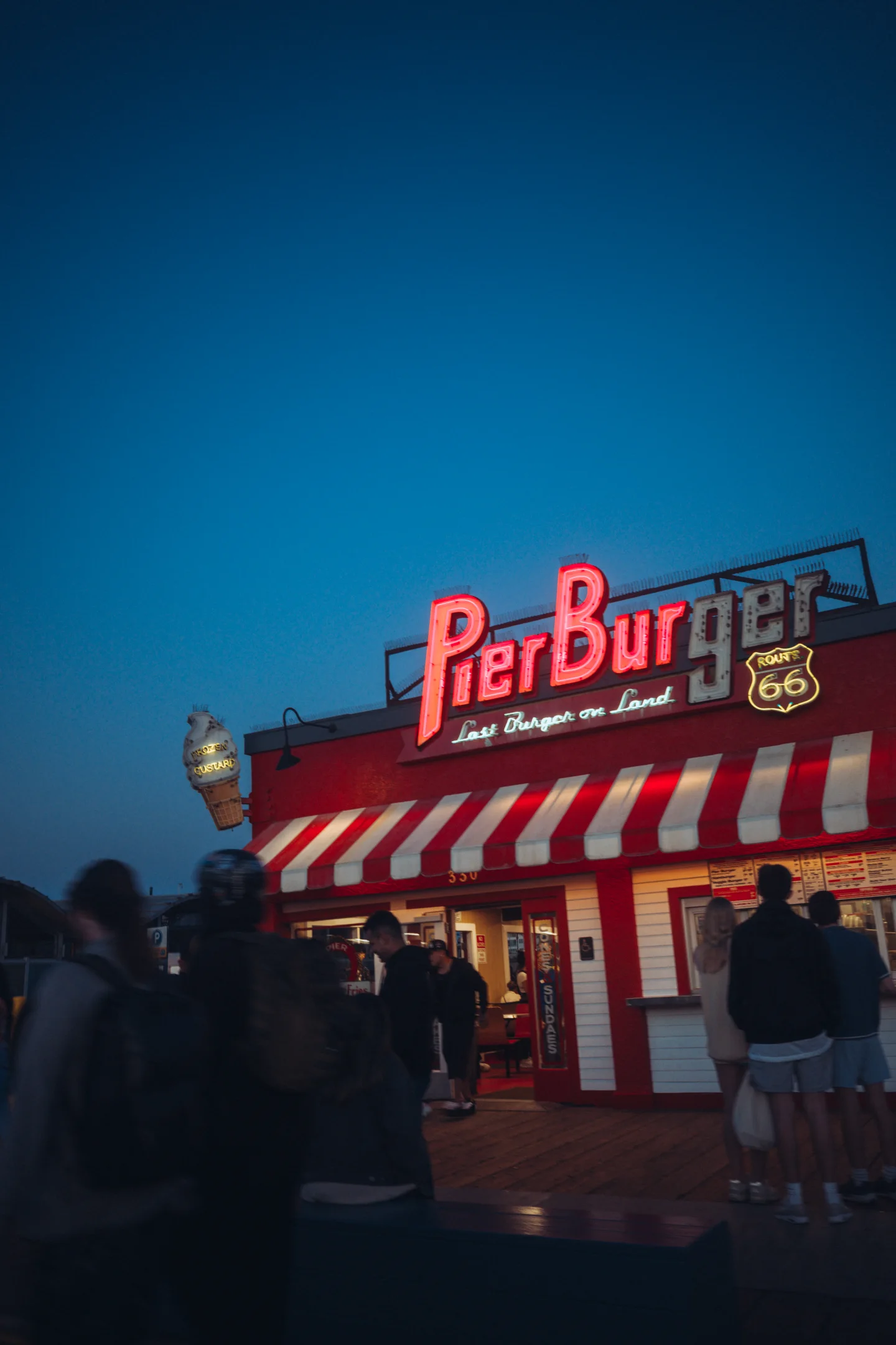 Red Pier Burger neon sign and visitors beneath a deep blue evening sky