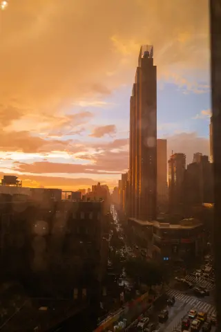 Orange storm clouds and a tall Manhattan tower above a wet avenue seen through a window.