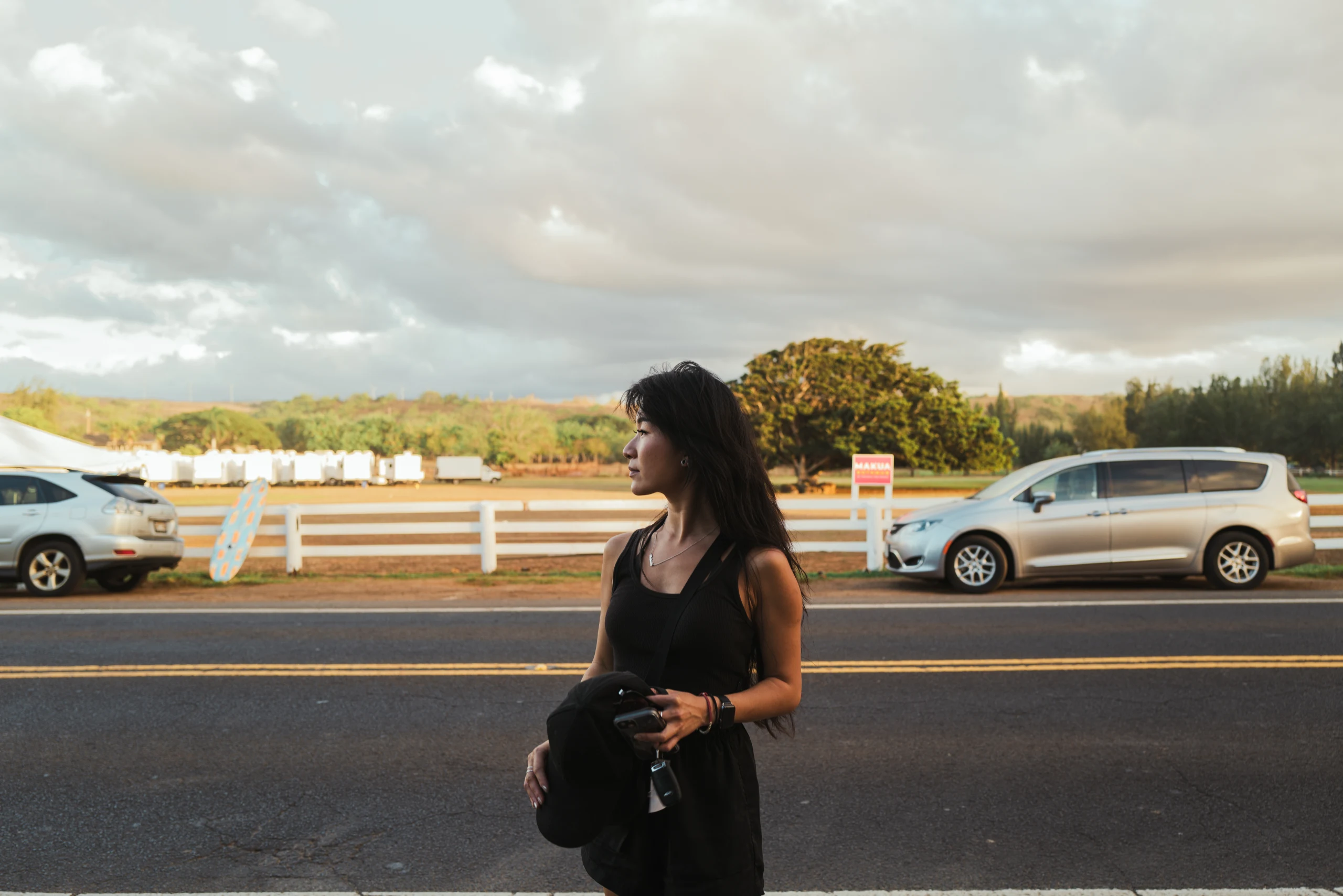 Woman dressed in black standing beside parked cars.