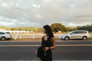 Woman dressed in black standing beside parked cars.