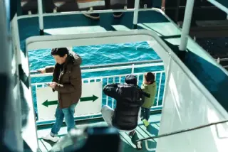 Passengers stand on the exterior stairs of a ferry.