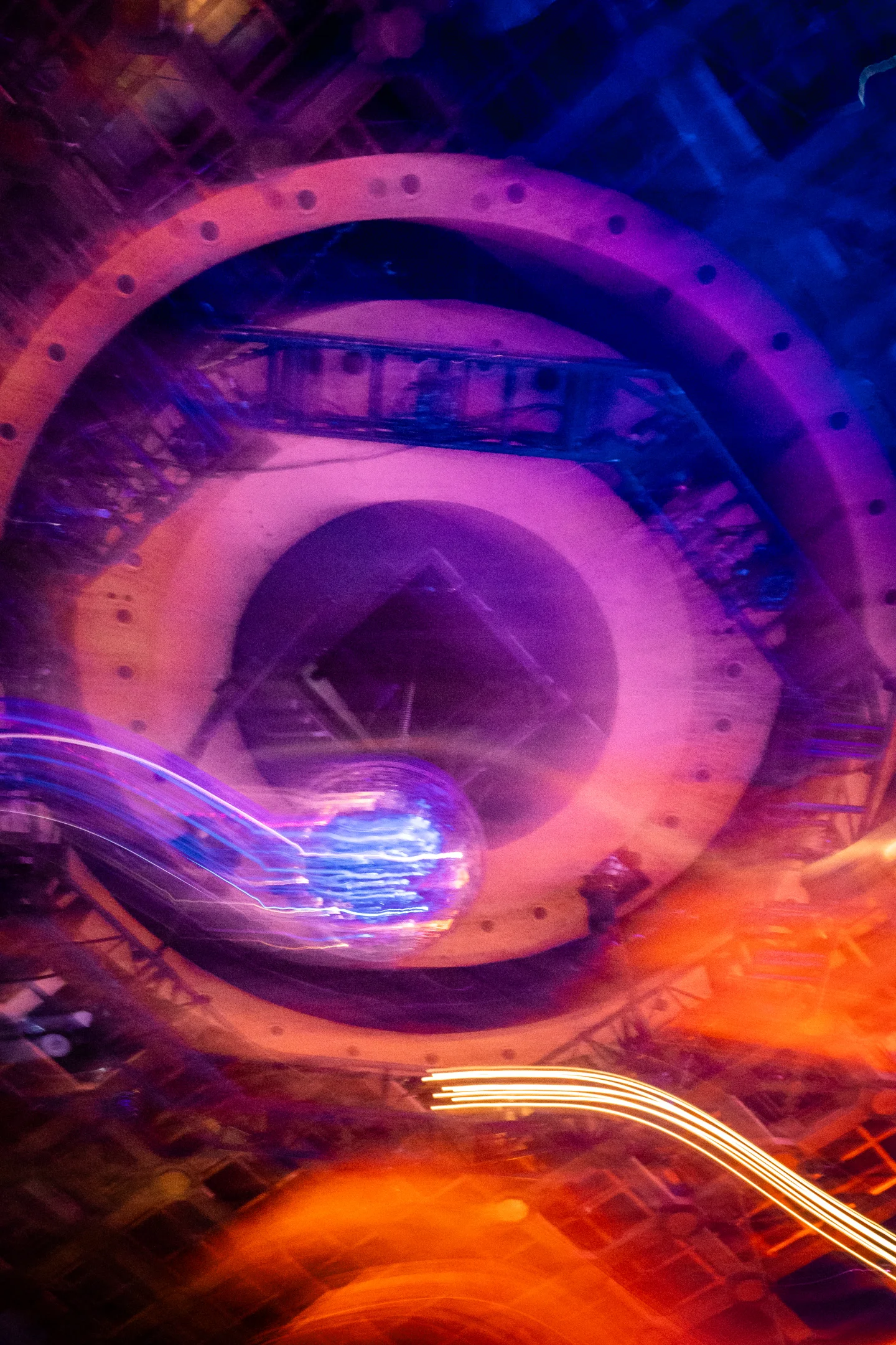 Long-exposure view of a mirrored ball and circular industrial ceiling in violet and orange light.