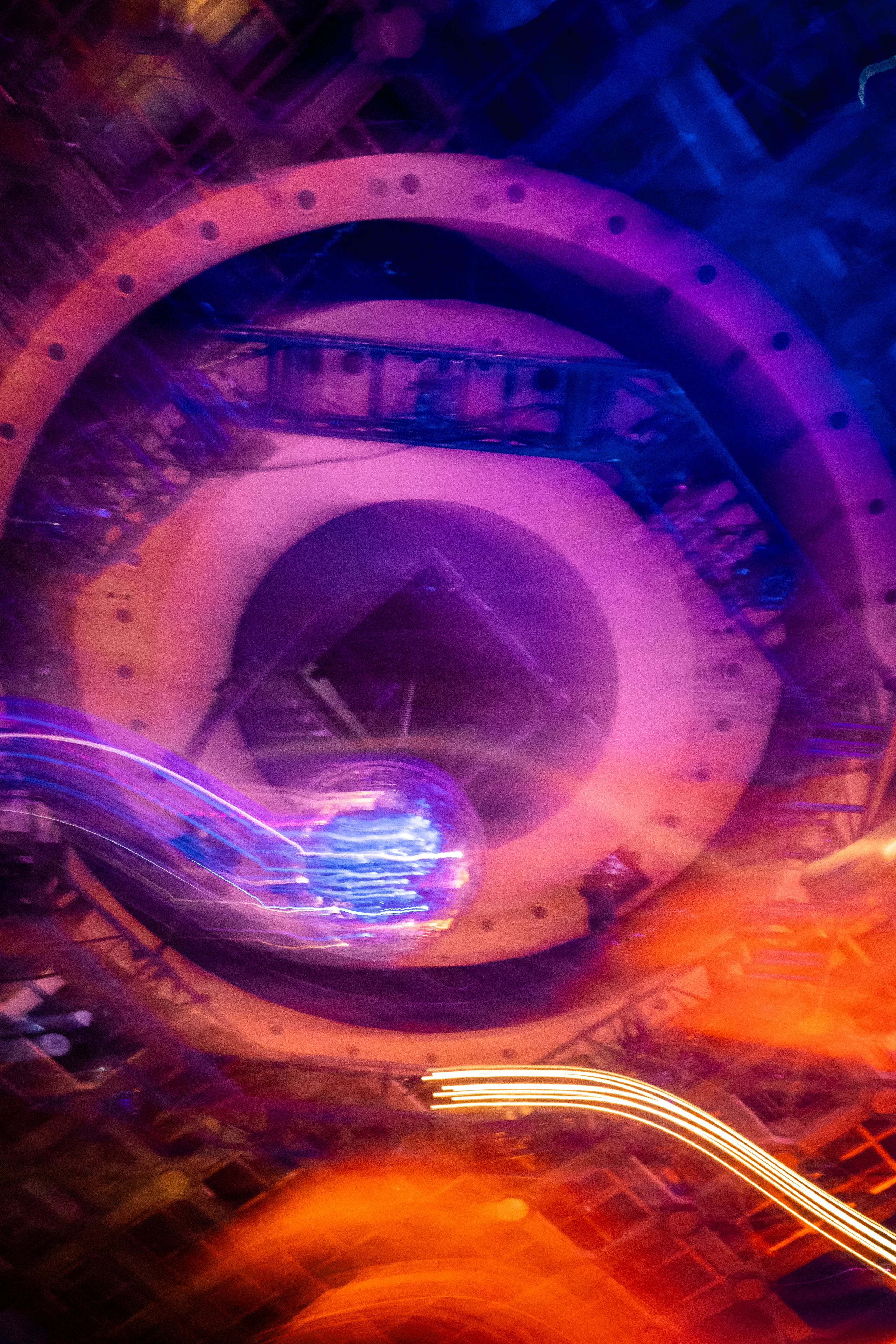 Long-exposure view of a mirrored ball and circular industrial ceiling in violet and orange light.