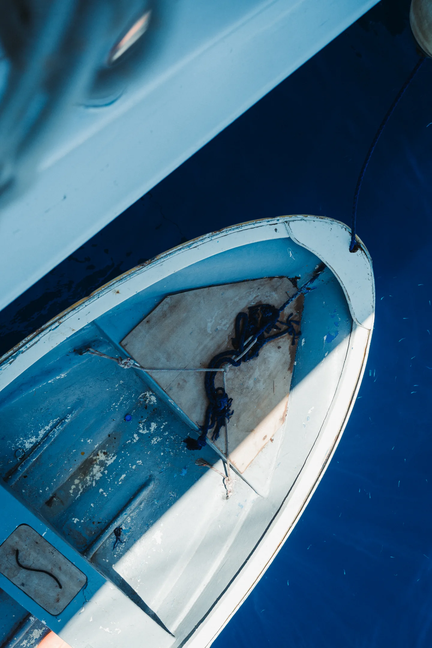 A weathered blue dinghy floats directly below in saturated navy water.