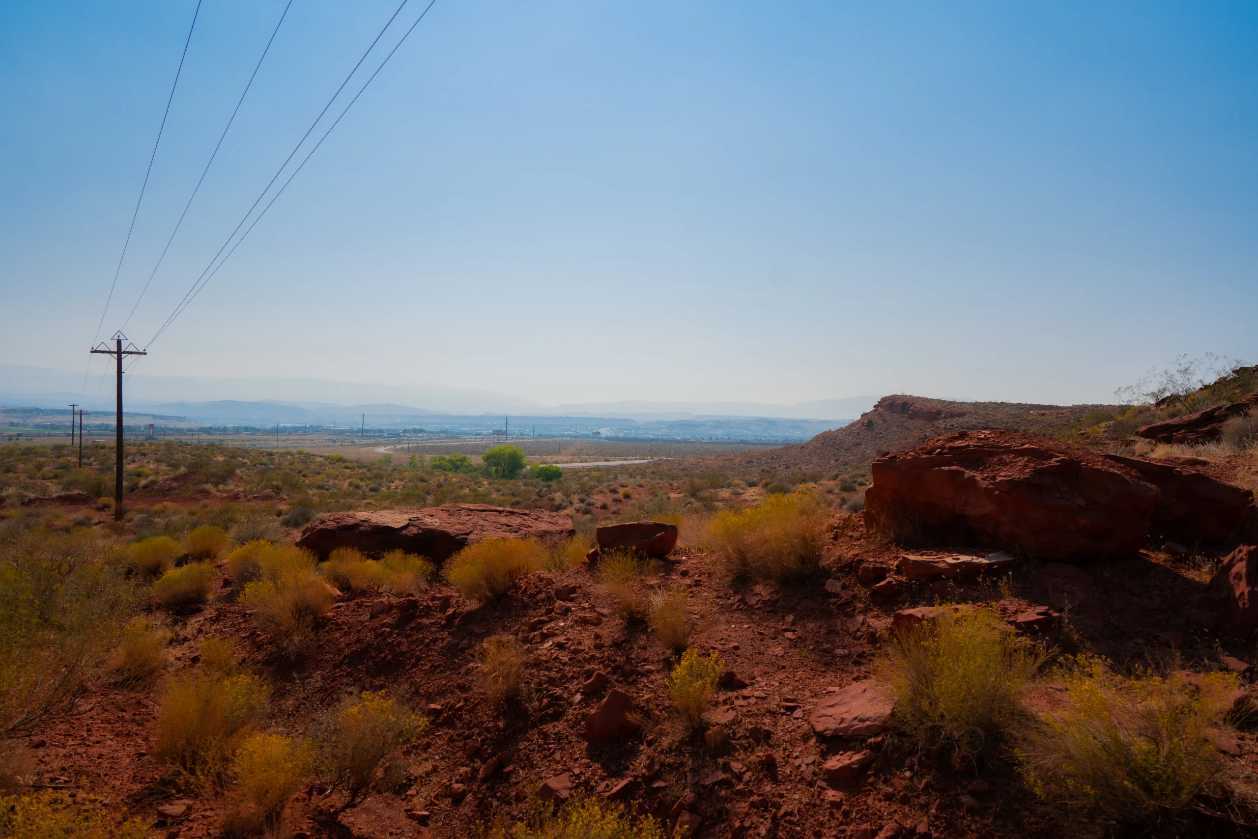 A road and utility poles lead toward sunlit red cliffs in Zion National Park.