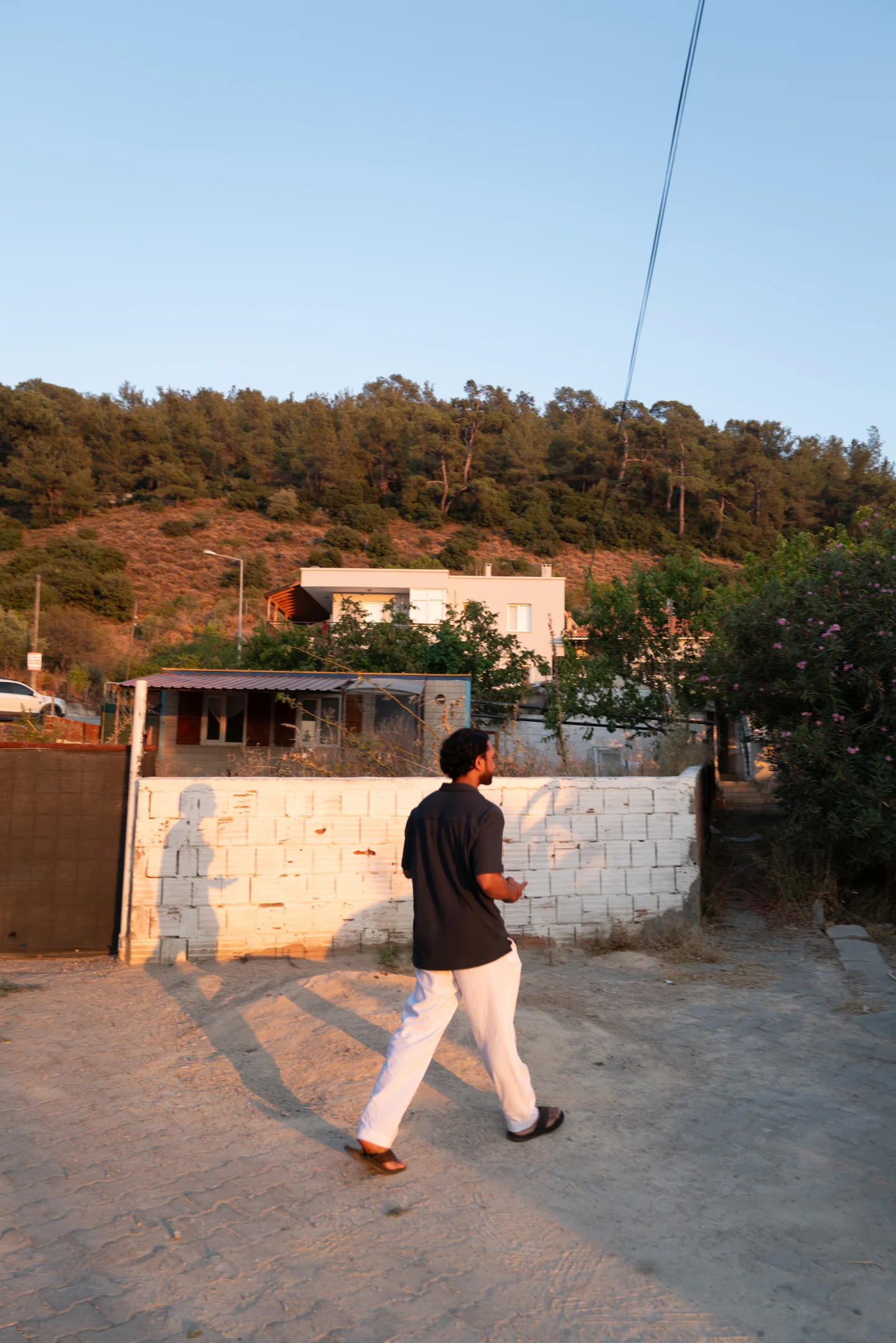 A man walks through a quiet village street in warm sunset light.