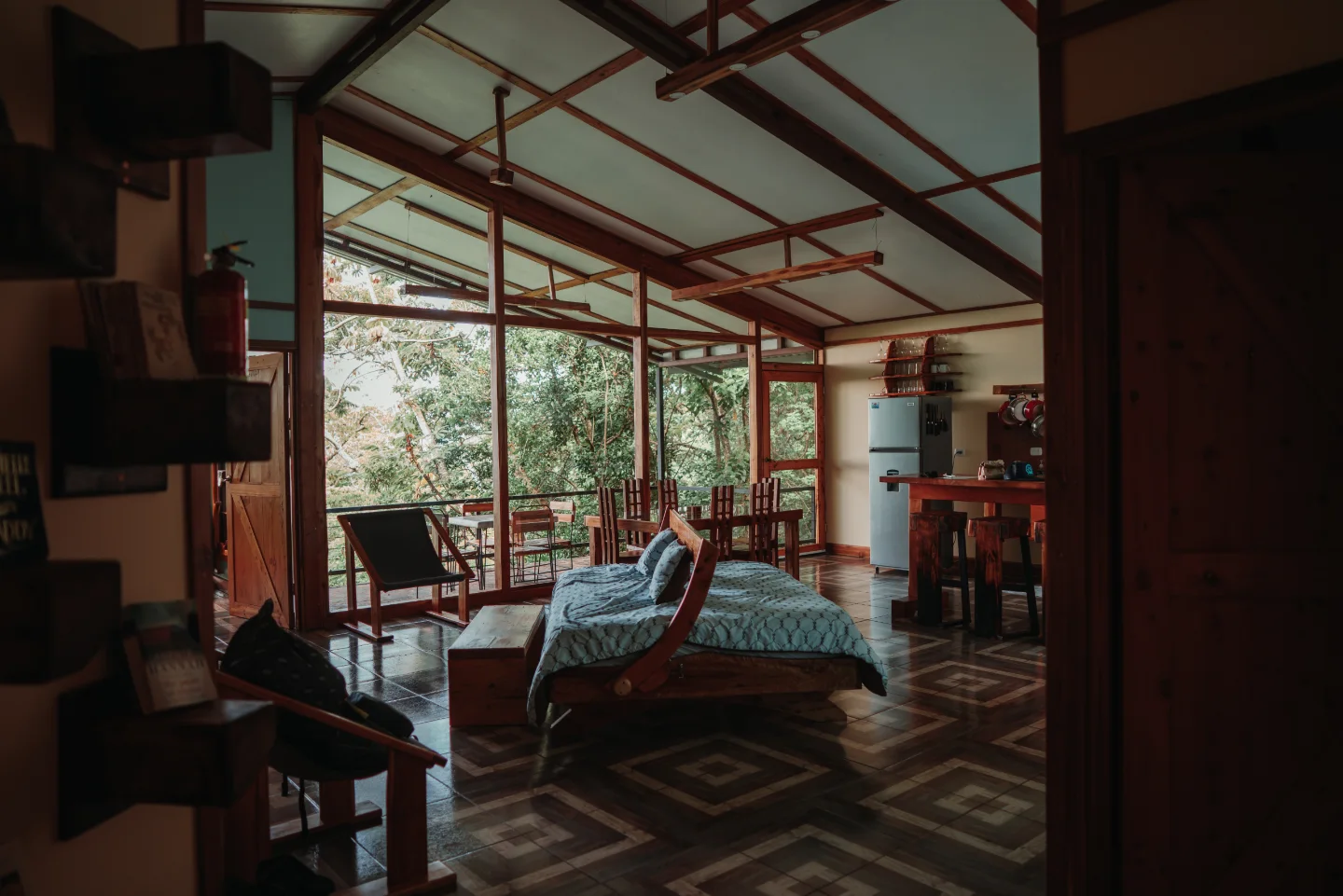 A wide open room looks through glass and timber toward the surrounding rainforest.