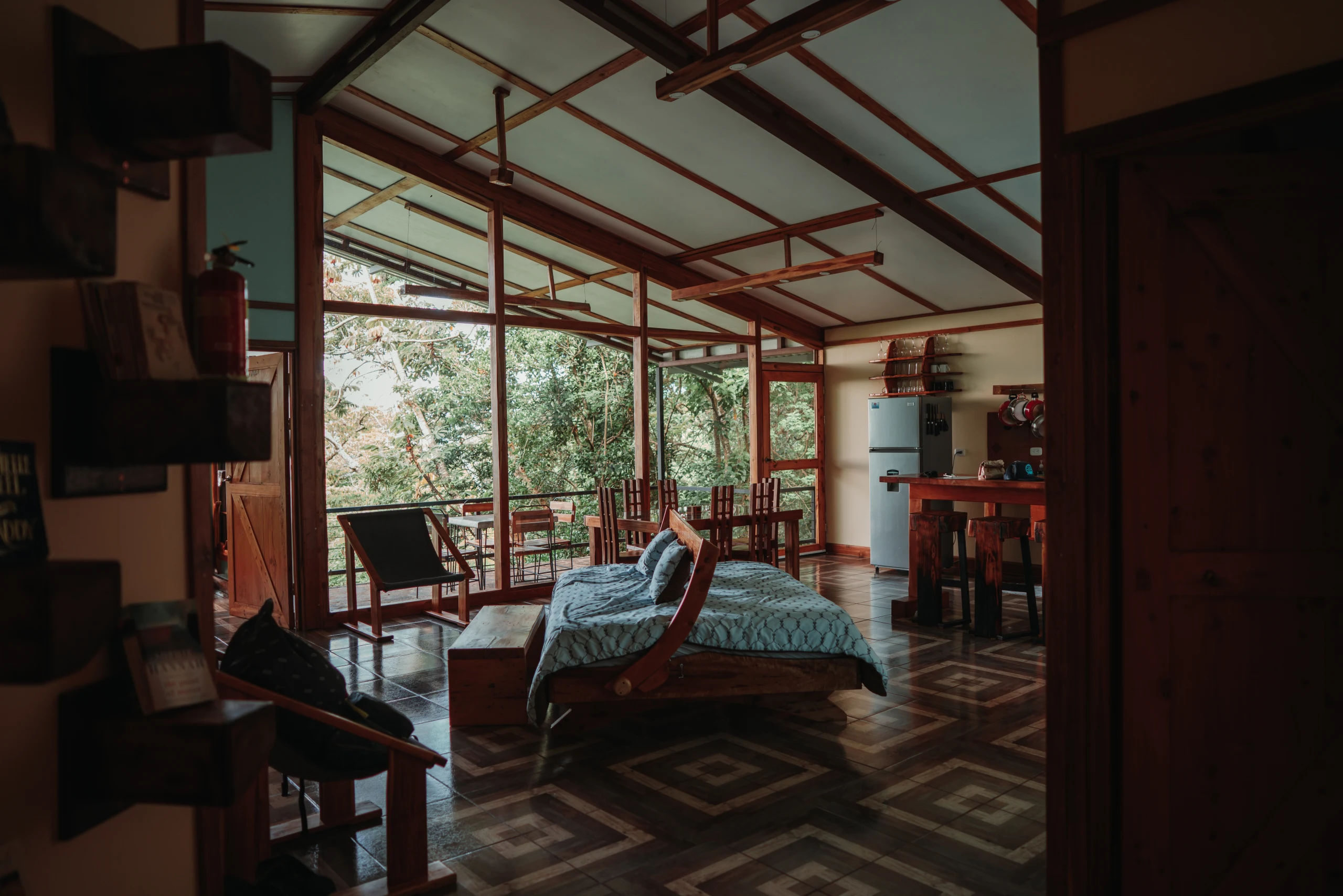 A wide open room looks through glass and timber toward the surrounding rainforest.
