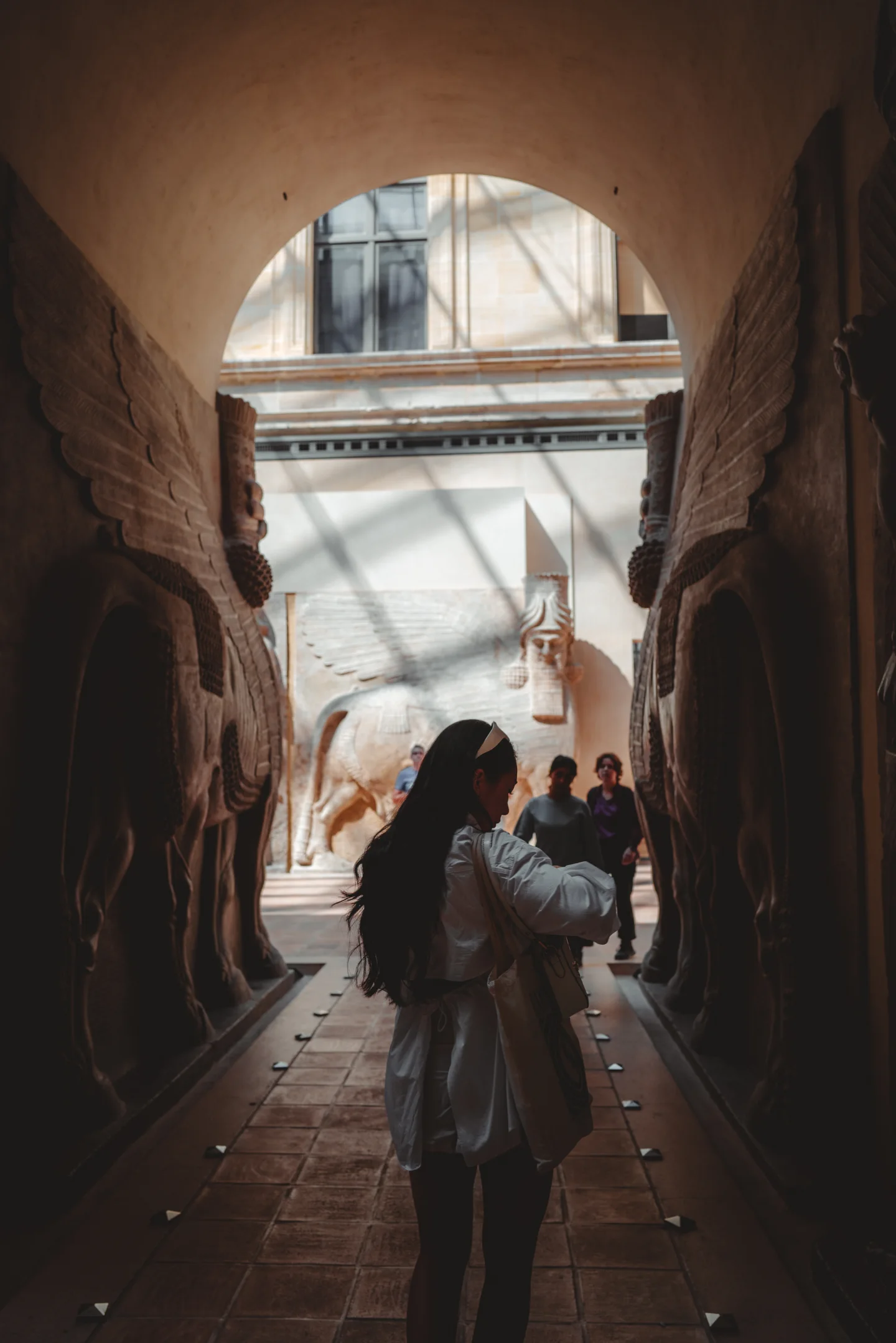 Figures framed by a shadowed arch at the Louvre.