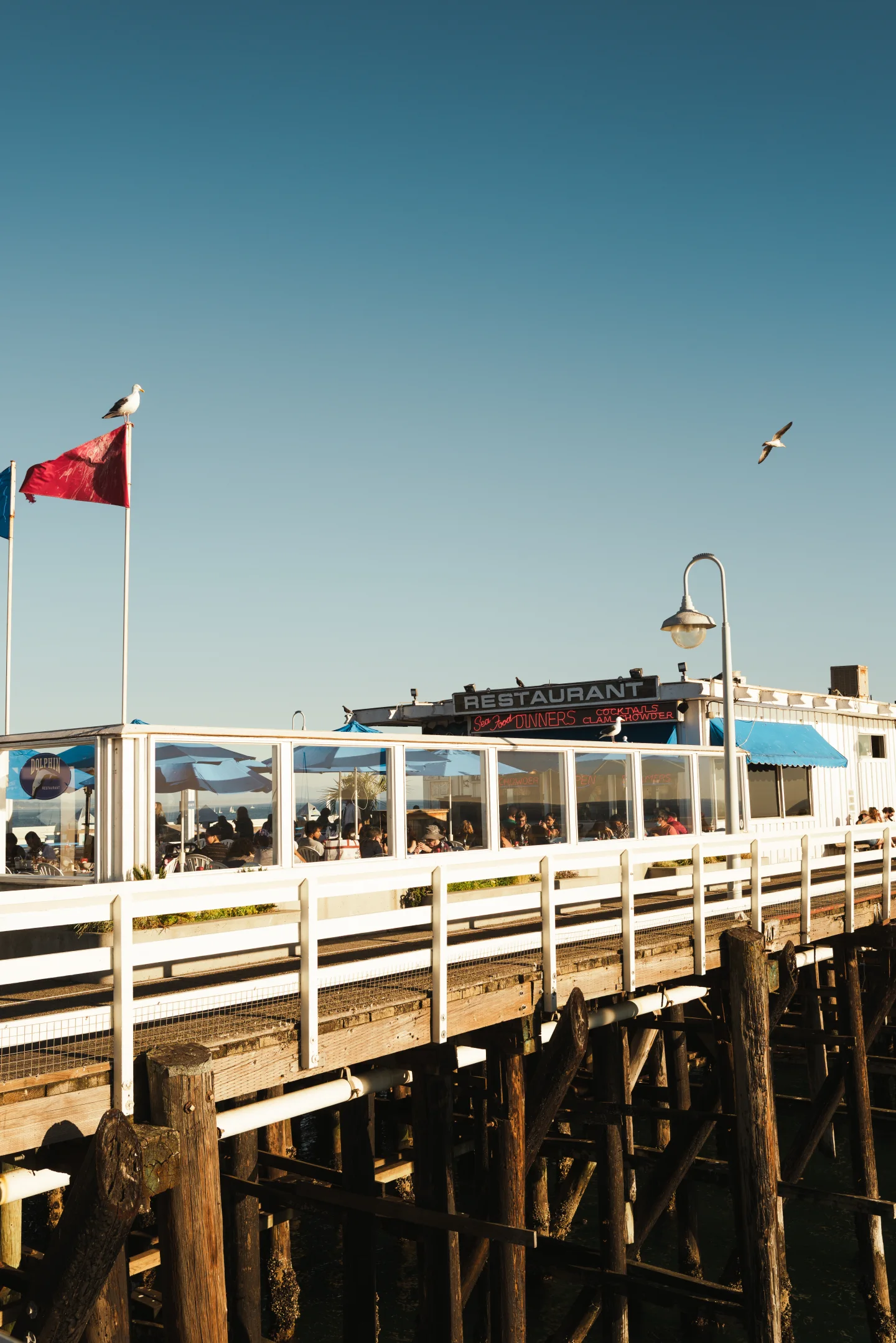 A red flag flying from a white pier structure against a pale blue sky.