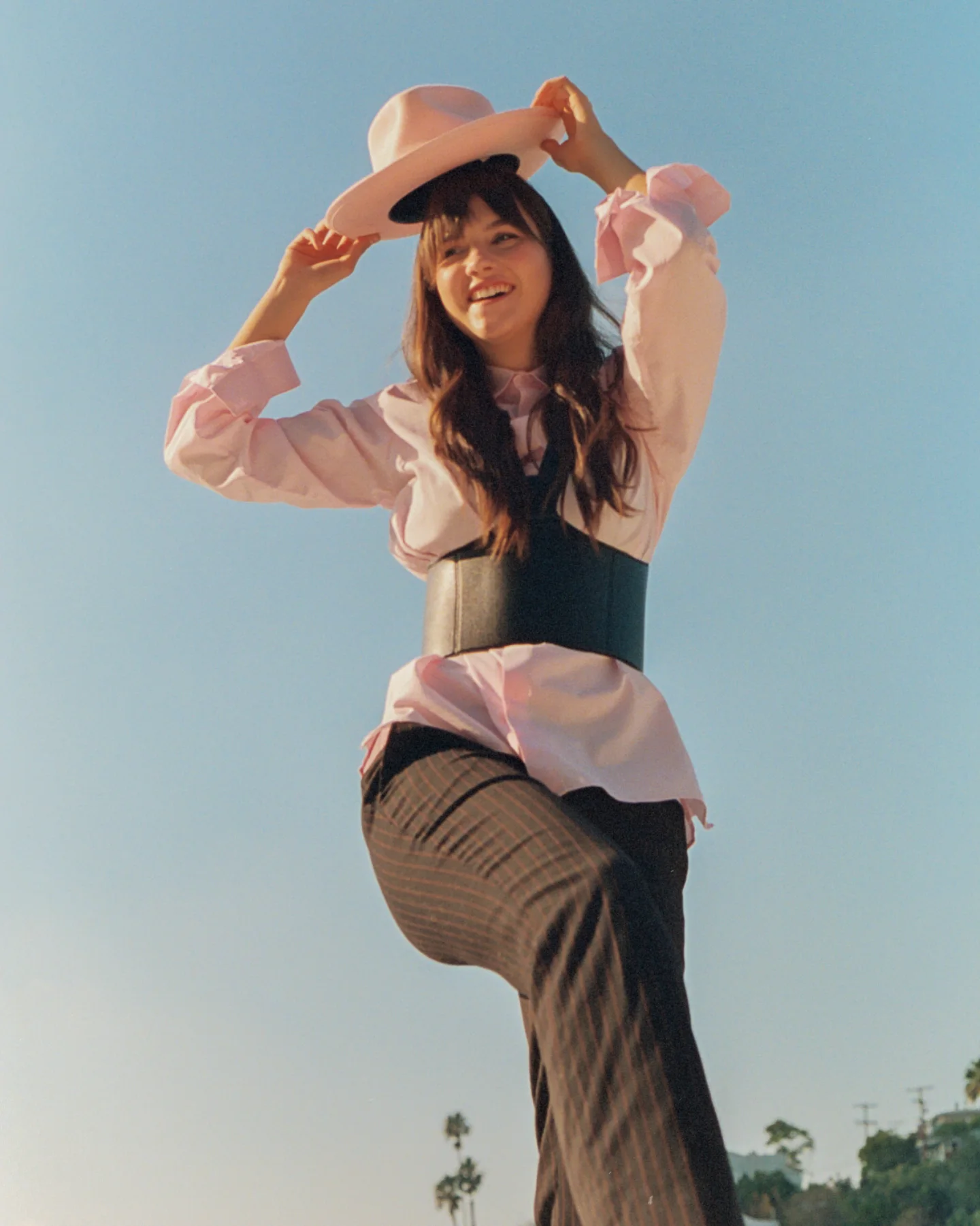 A woman in a pale pink hat and layered clothing posing against a clear blue sky.