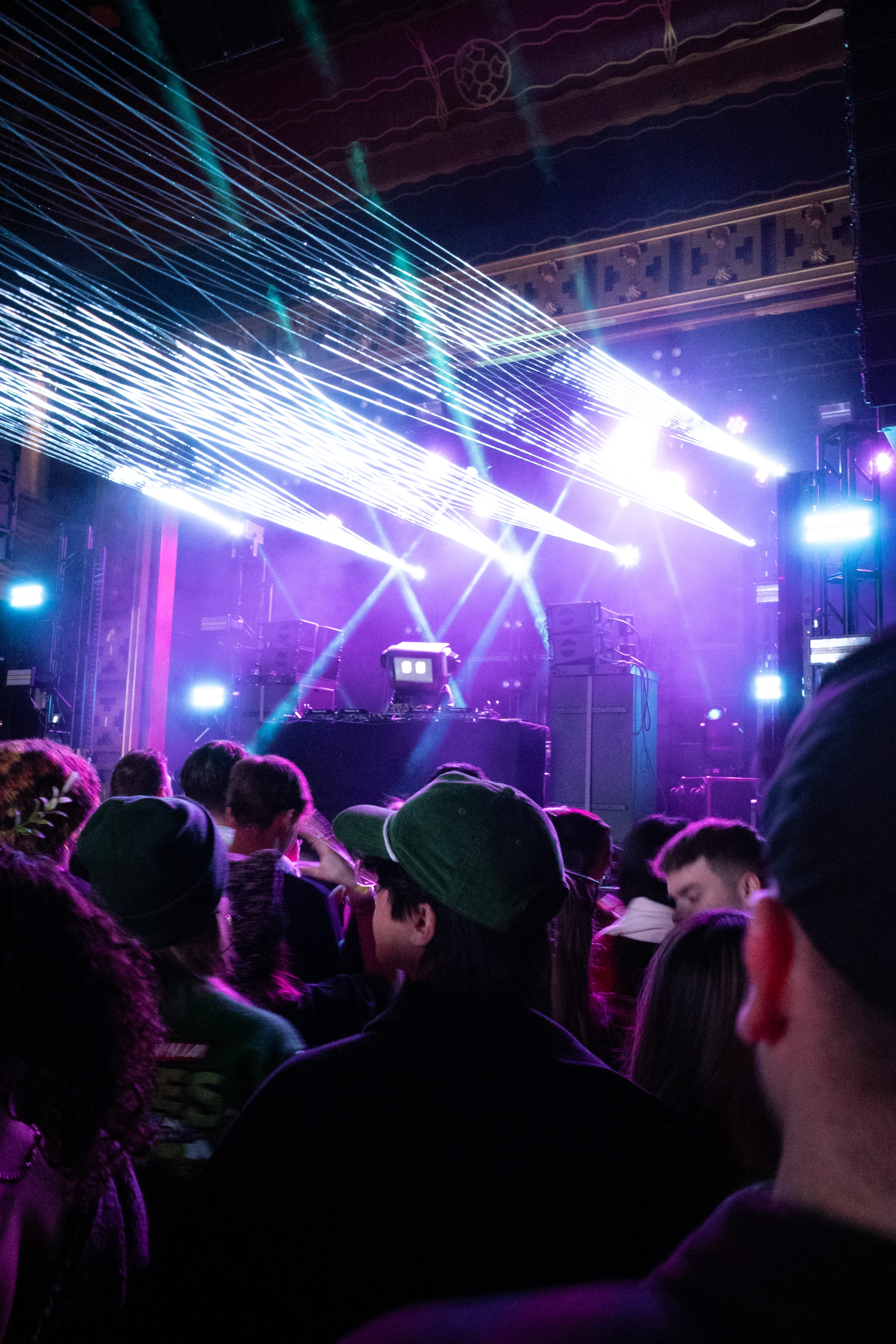 Crowd beneath bright white laser lines and violet stage lighting inside a Brooklyn venue.