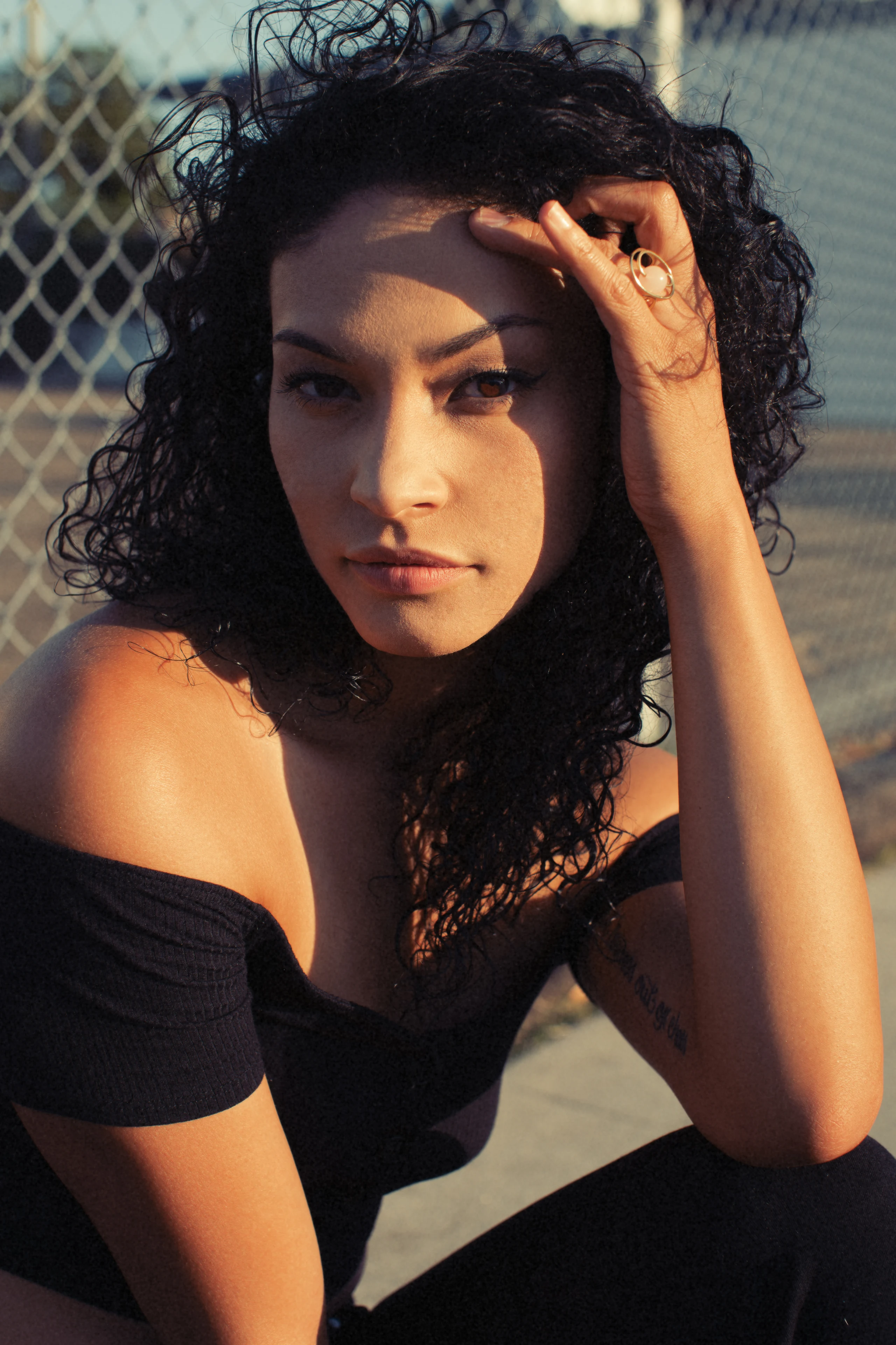 Close portrait of a seated woman in black raising one hand against bright sun.