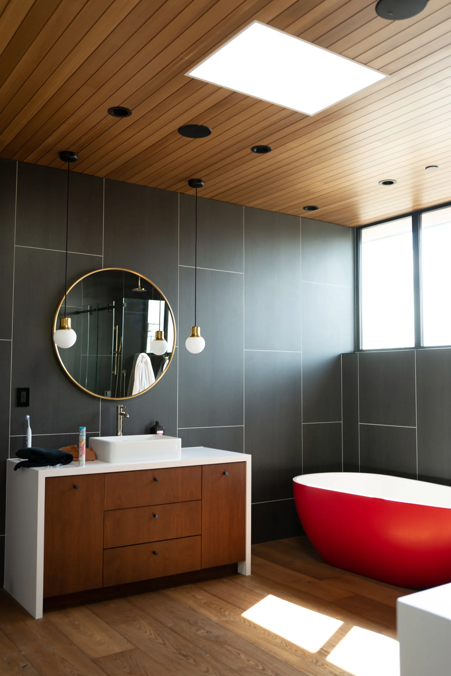A red freestanding bathtub sits in a wood-and-tile bathroom.