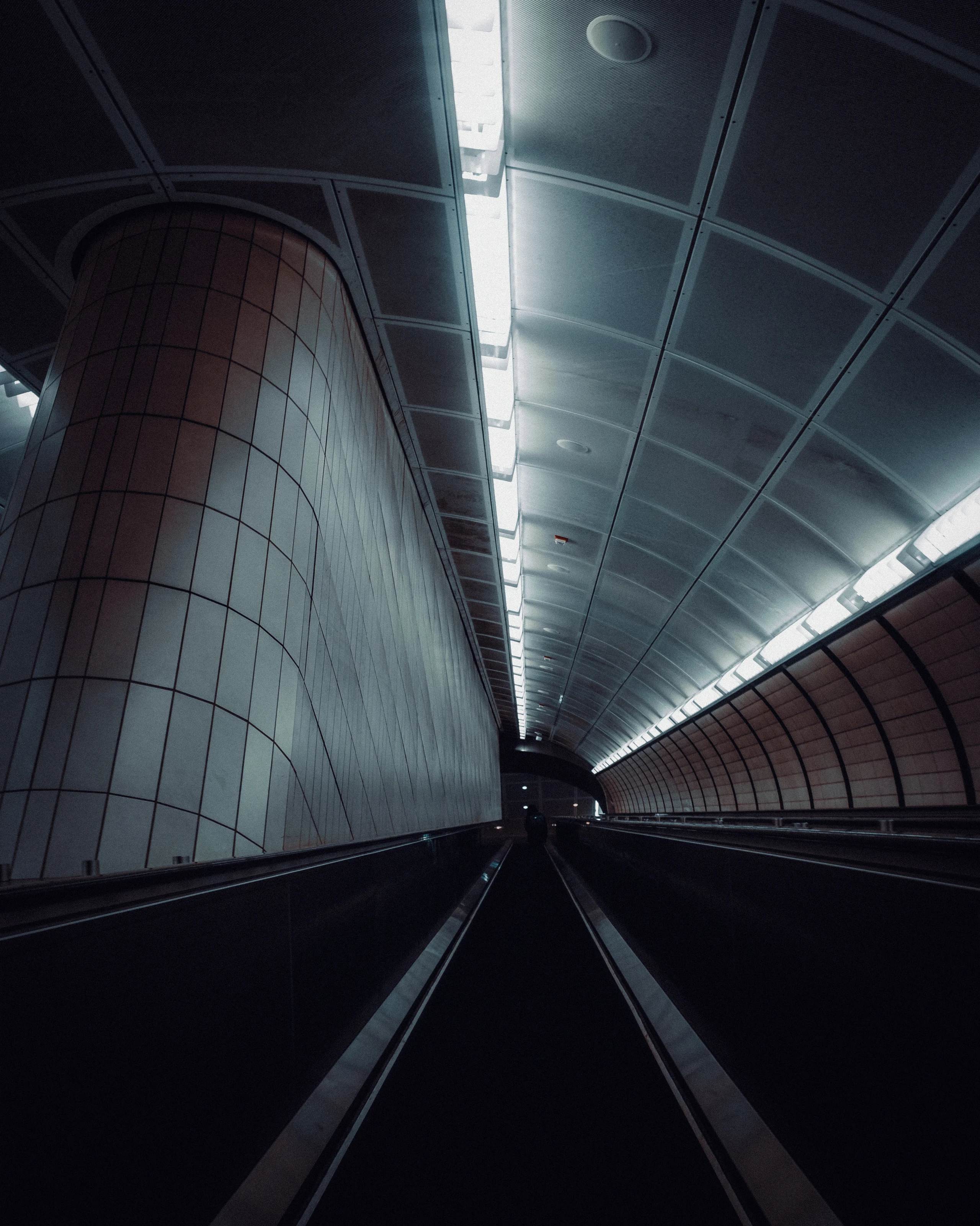 Empty curved subway escalator descending beneath fluorescent lights